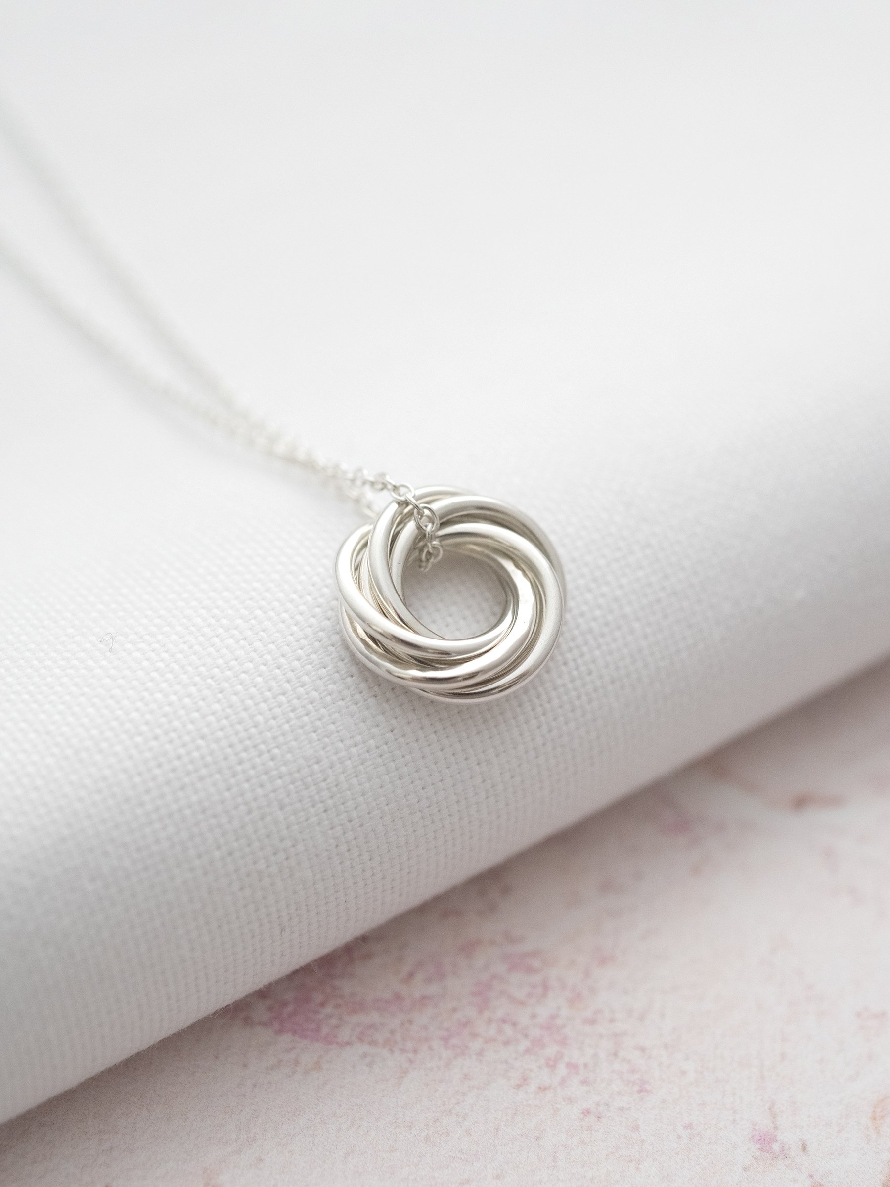 A side view of a silver 6 ring necklace for 60th birthday displayed over white material.