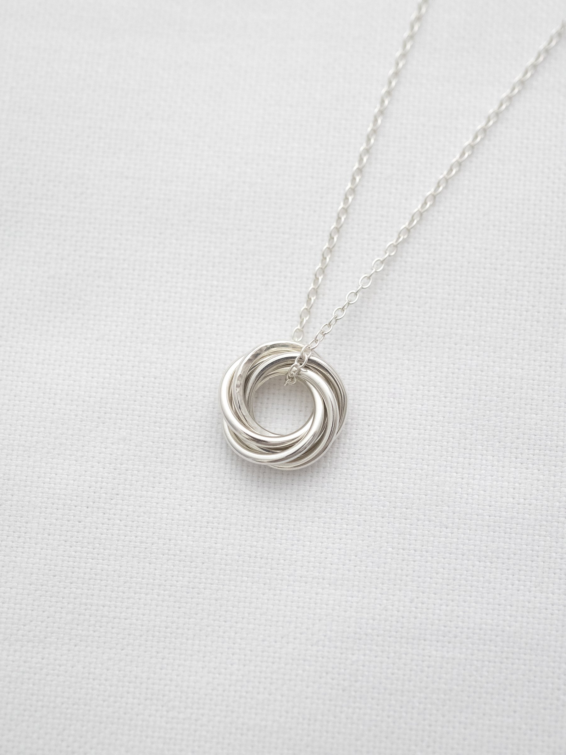A sterling silver 6 ring necklace displayed on white material.