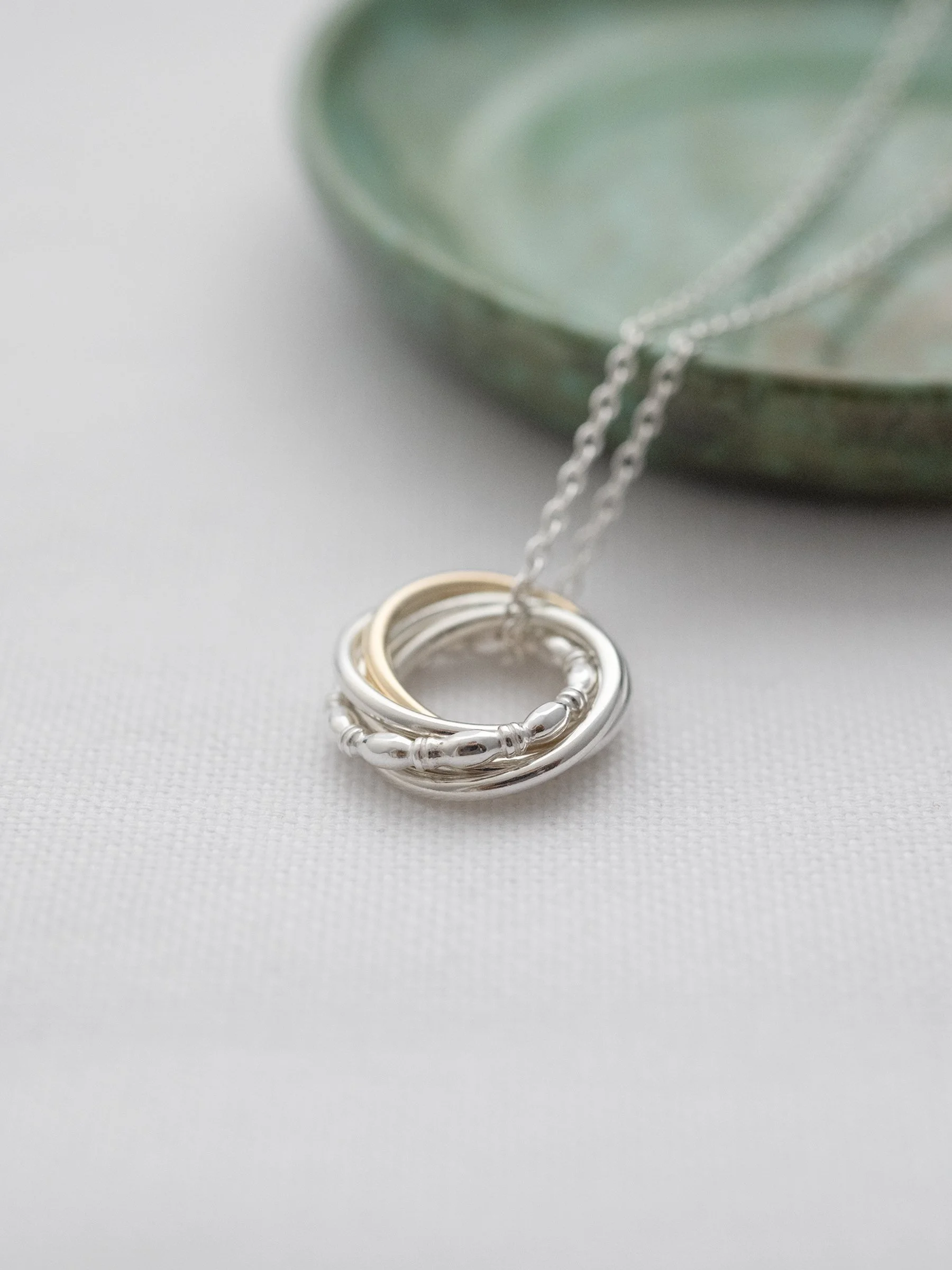 A luxury 50th gold and silver birthday necklace displayed on white material with a green jewellery dish in the background.