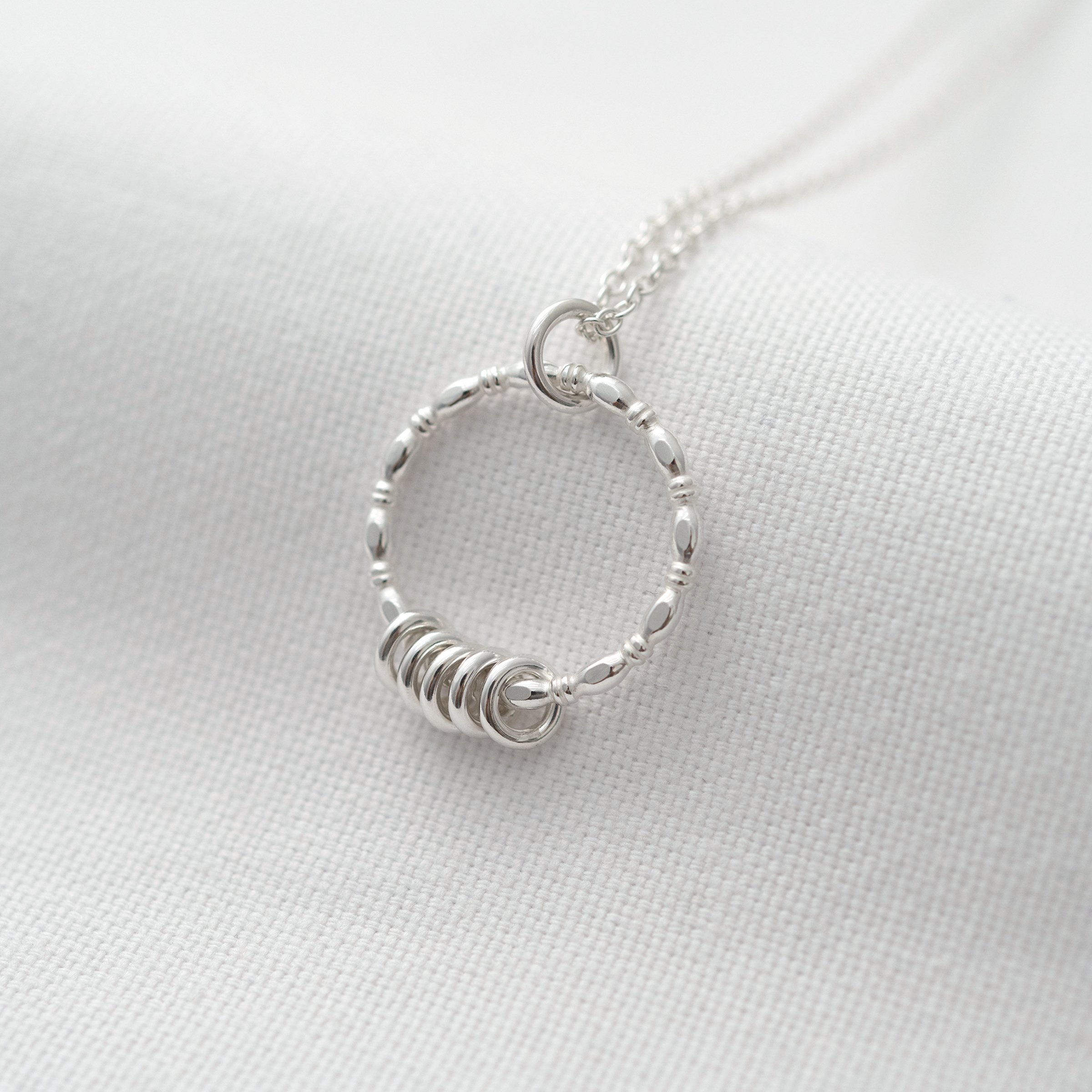 A slight side view of a silver 50th ring necklace displayed over white material.