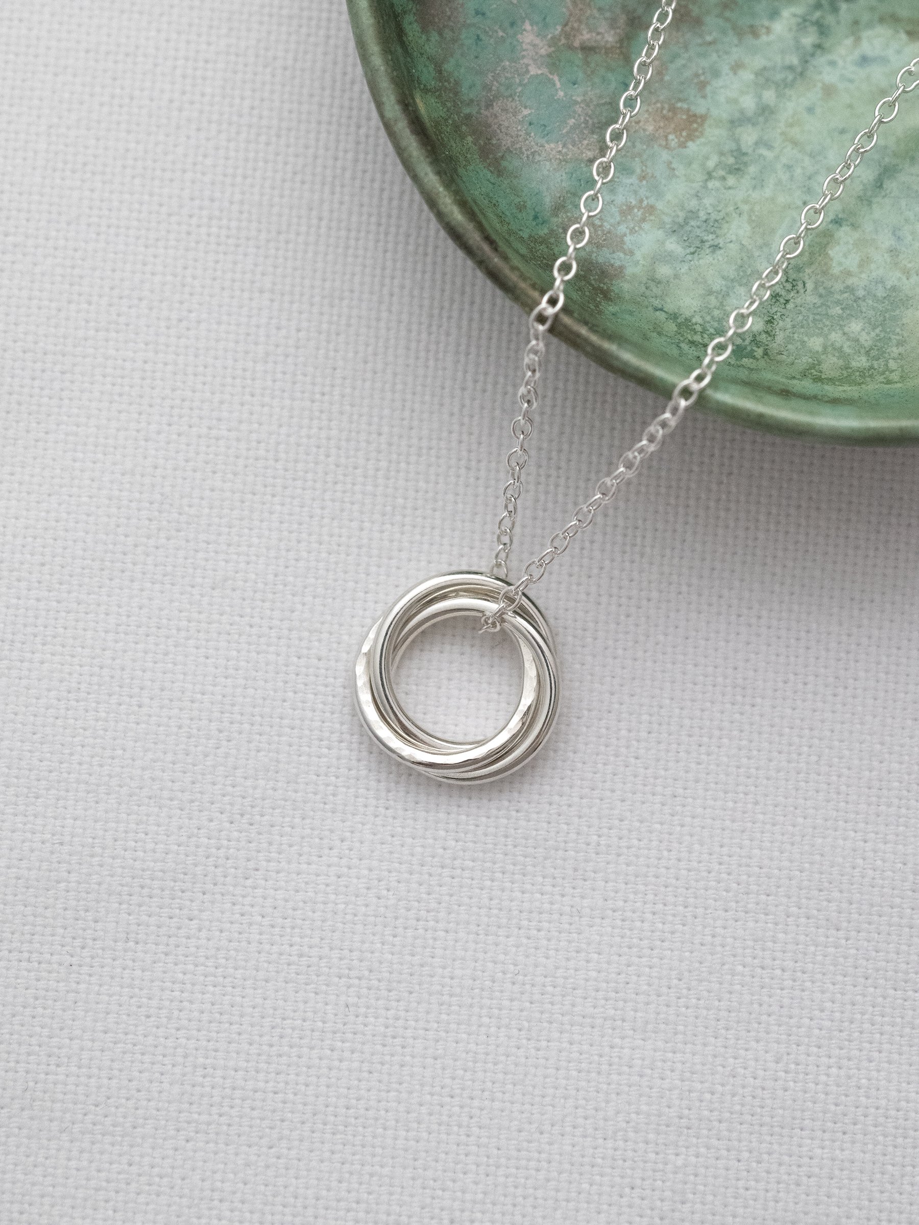 A sterling silver 3 ring necklace for a 30th birthday displayed on white material with a green jewellery dish in the background.