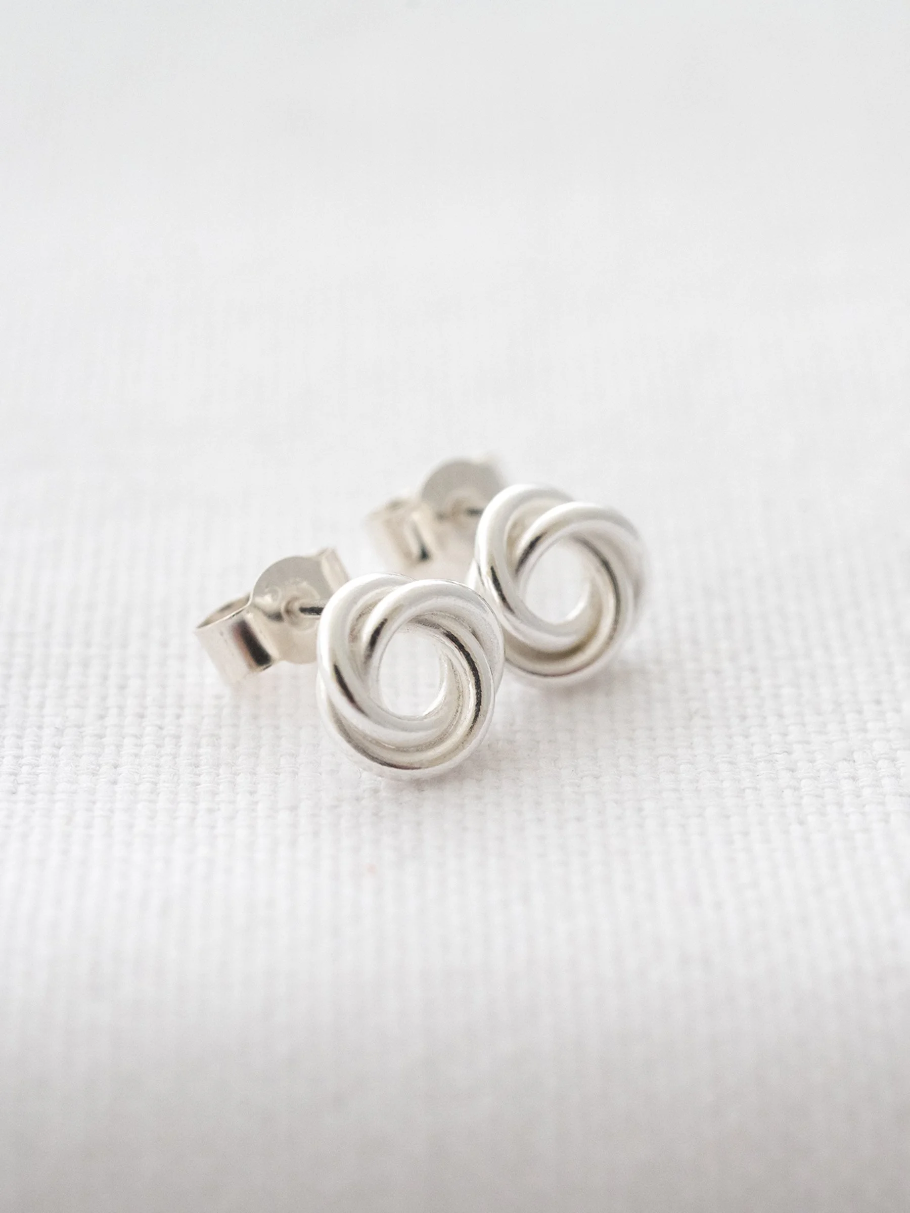 A side view of a pair of silver 30th birthday stud earrings displayed over white material.