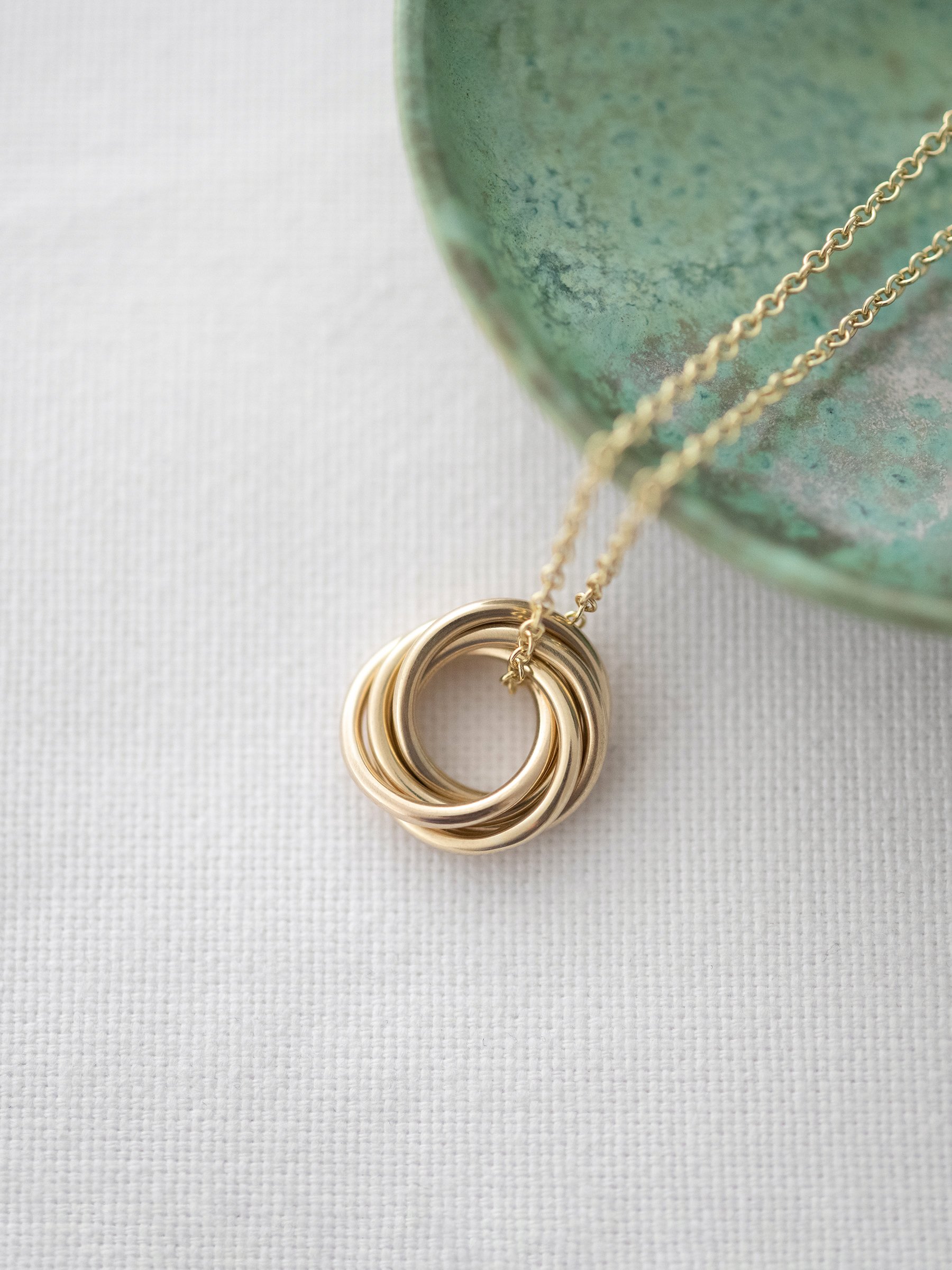 A 9ct gold 50th birthday necklace displayed over white material and a green jewellery dish.