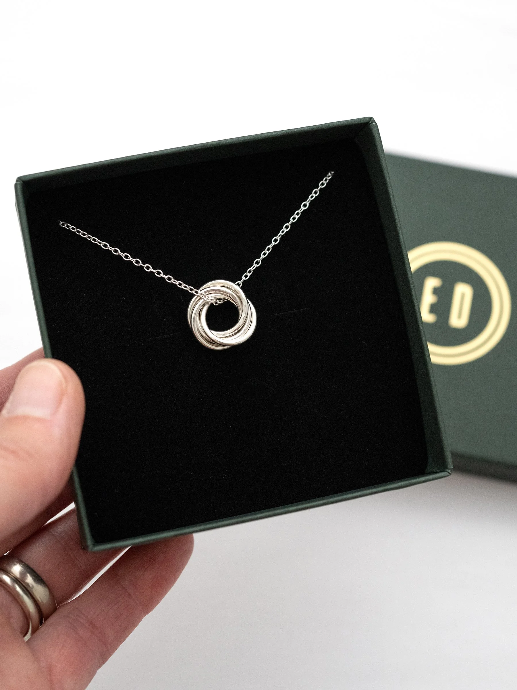 A silver fiver ring necklace displayed in a jewellery presentation box.