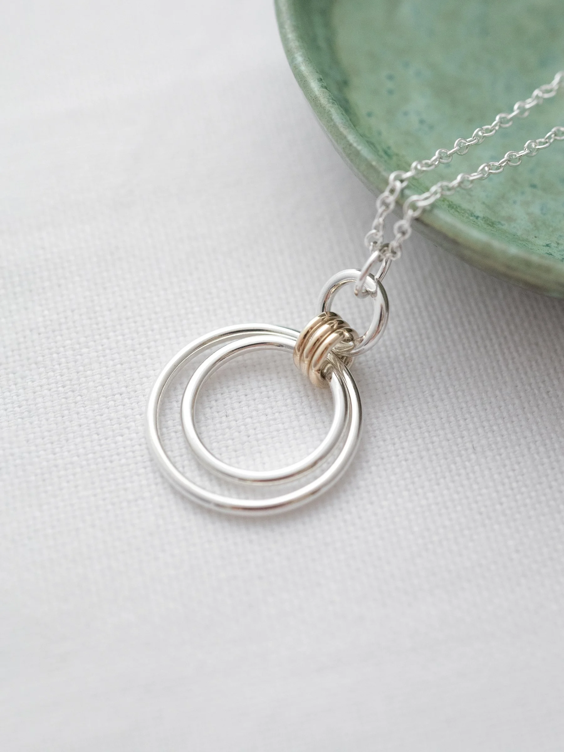 A close up of a 30th gold and silver birthday necklace displayed on white material with a green jewellery dish in the background.