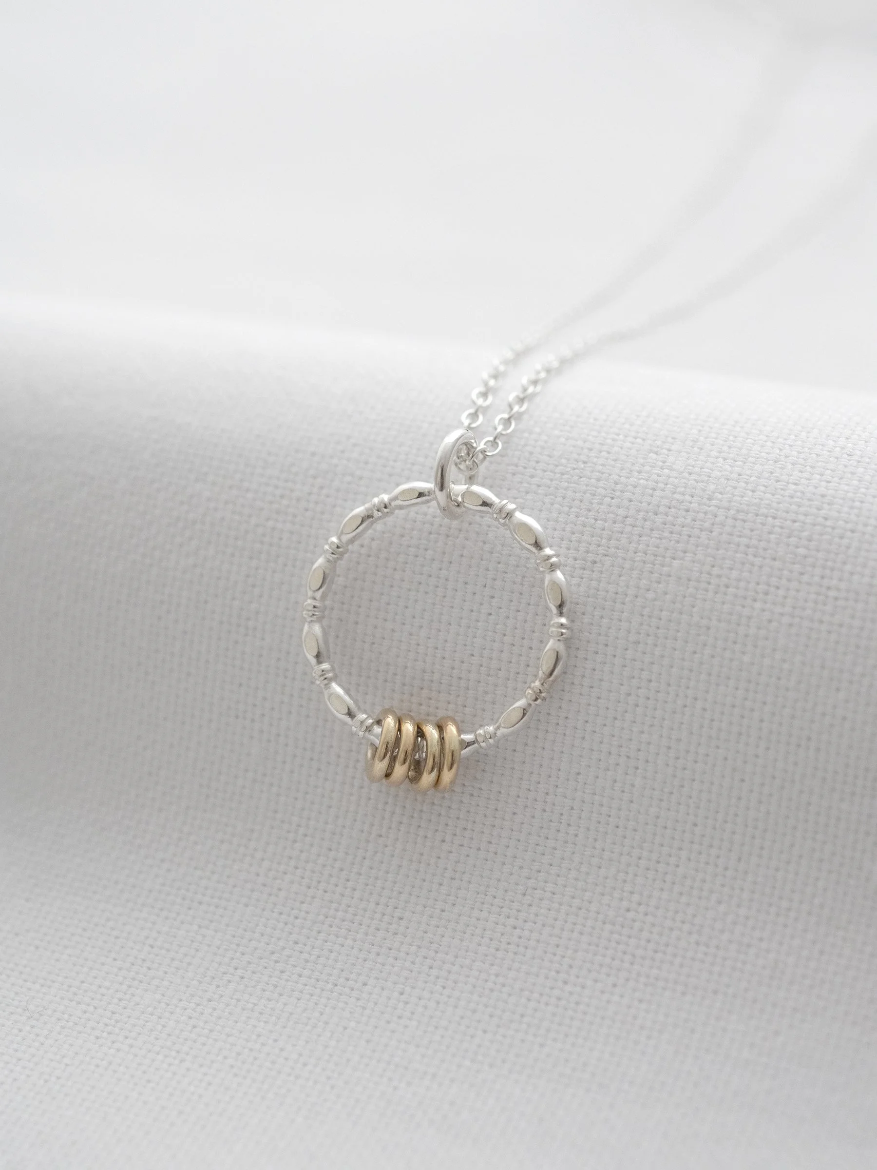 A gold and silver four ring necklace displayed over white material.