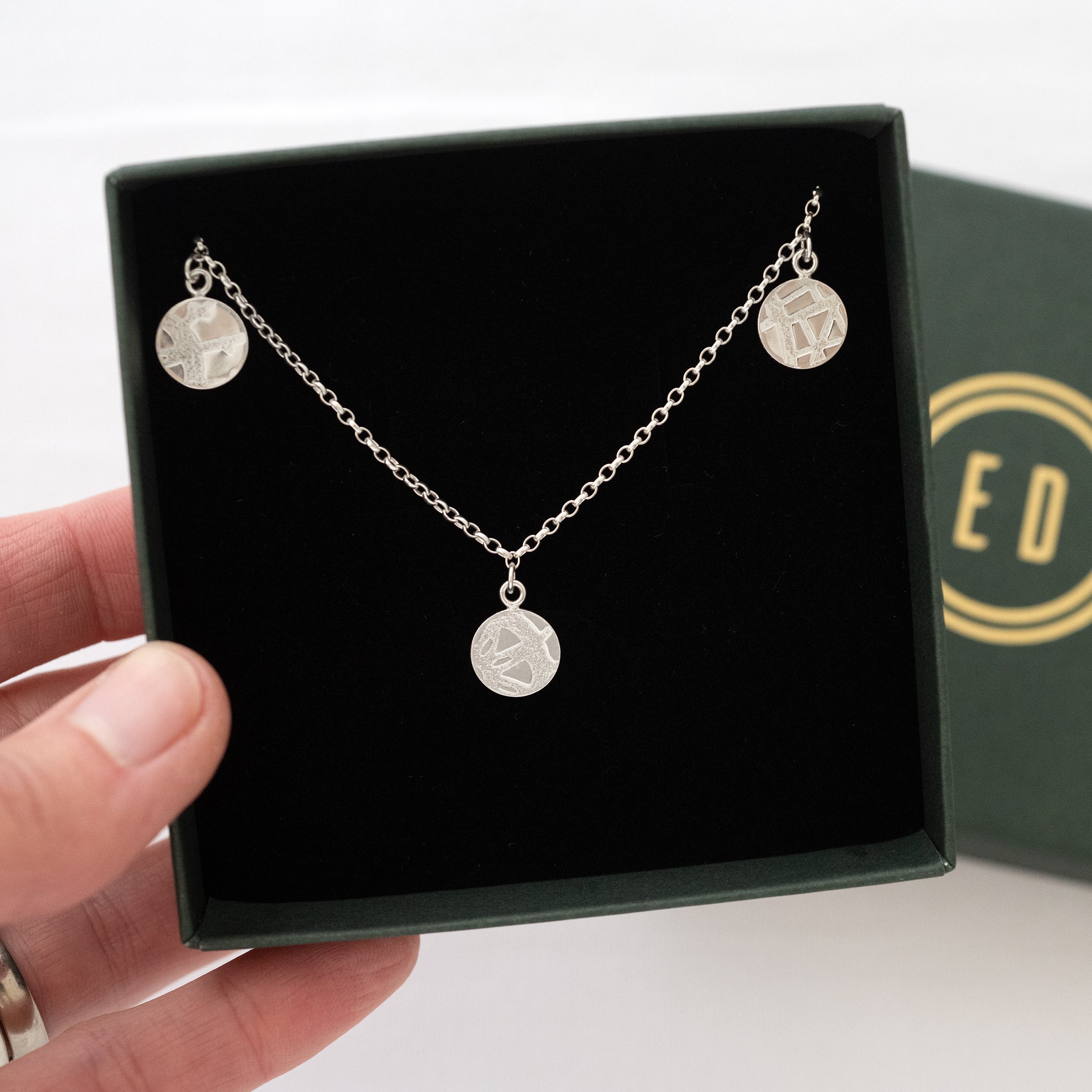 A silver circle disc necklace displayed in a green presentation box.