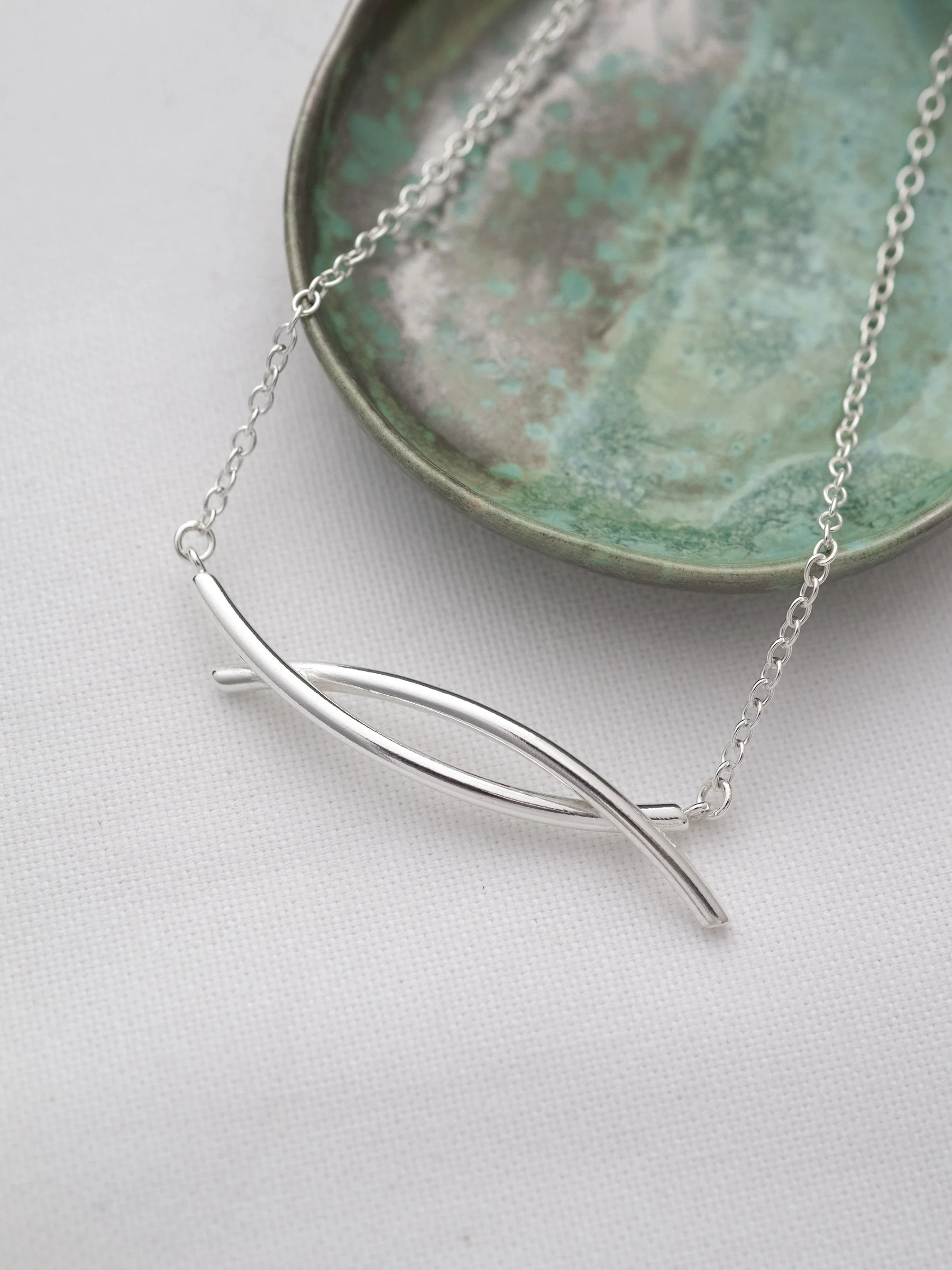 A close up of a silver entwined twist necklace with a green jewellery dish in the background.