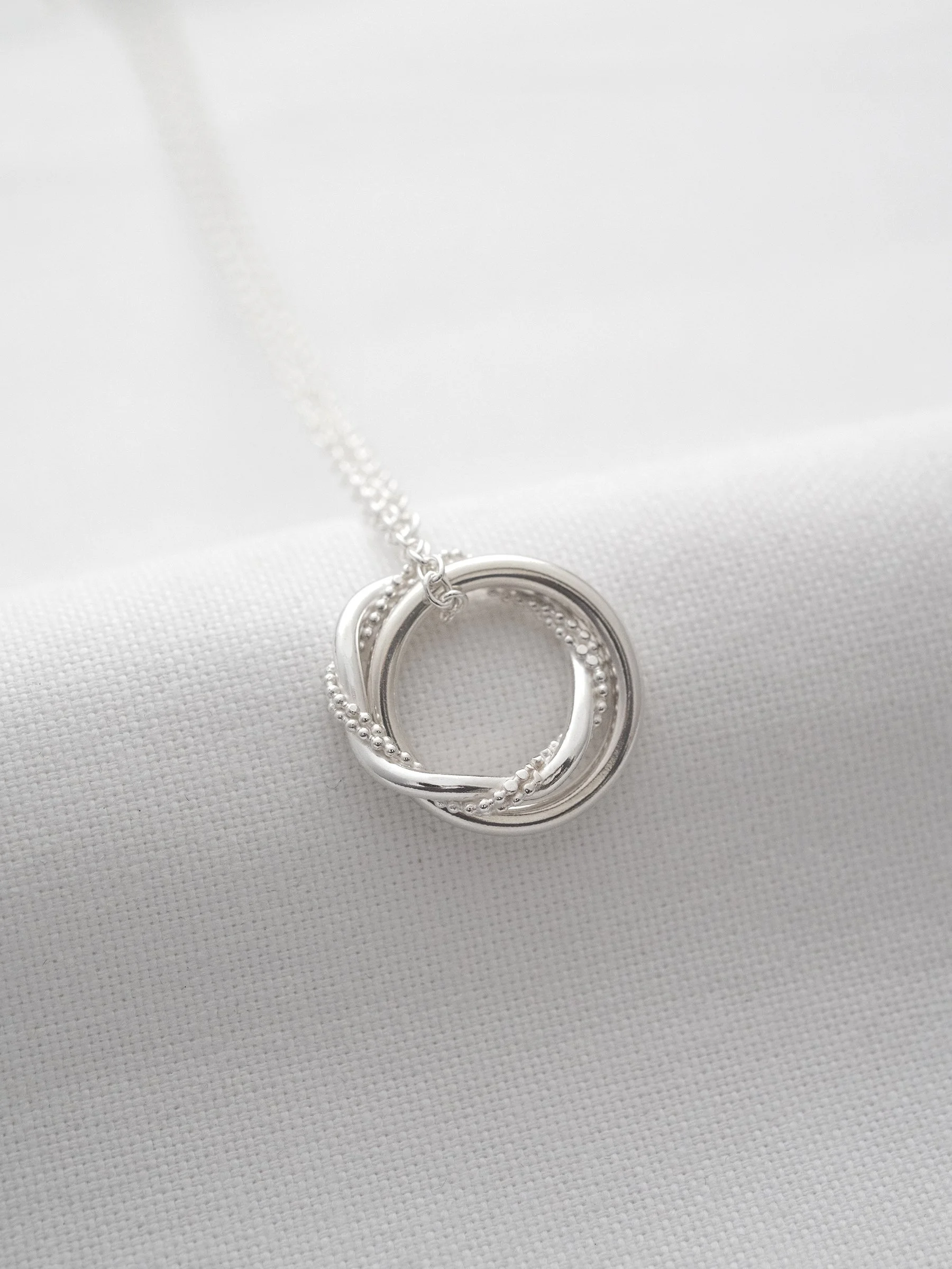 A sterling silver unique two ring necklace displayed over white material.
