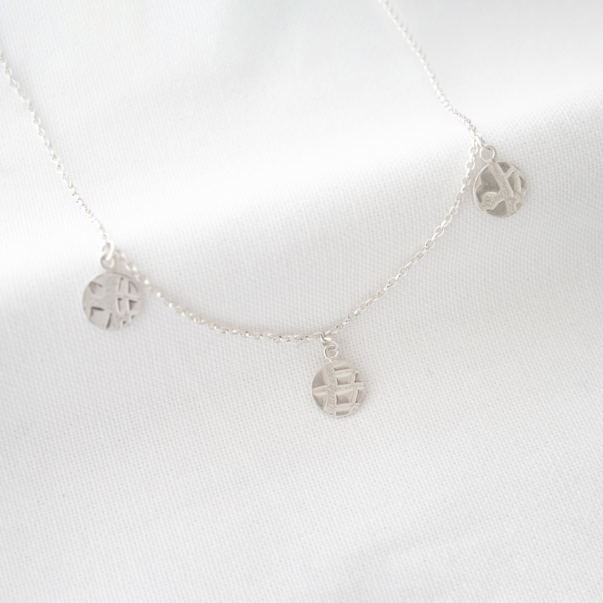 Sterling silver disc necklace displayed over white material.