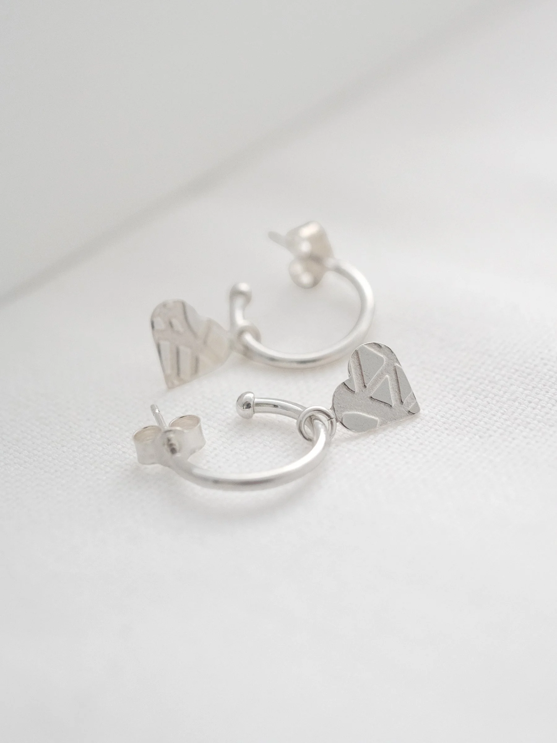 A pair of heart pattern hoop stud earring displayed on white material.