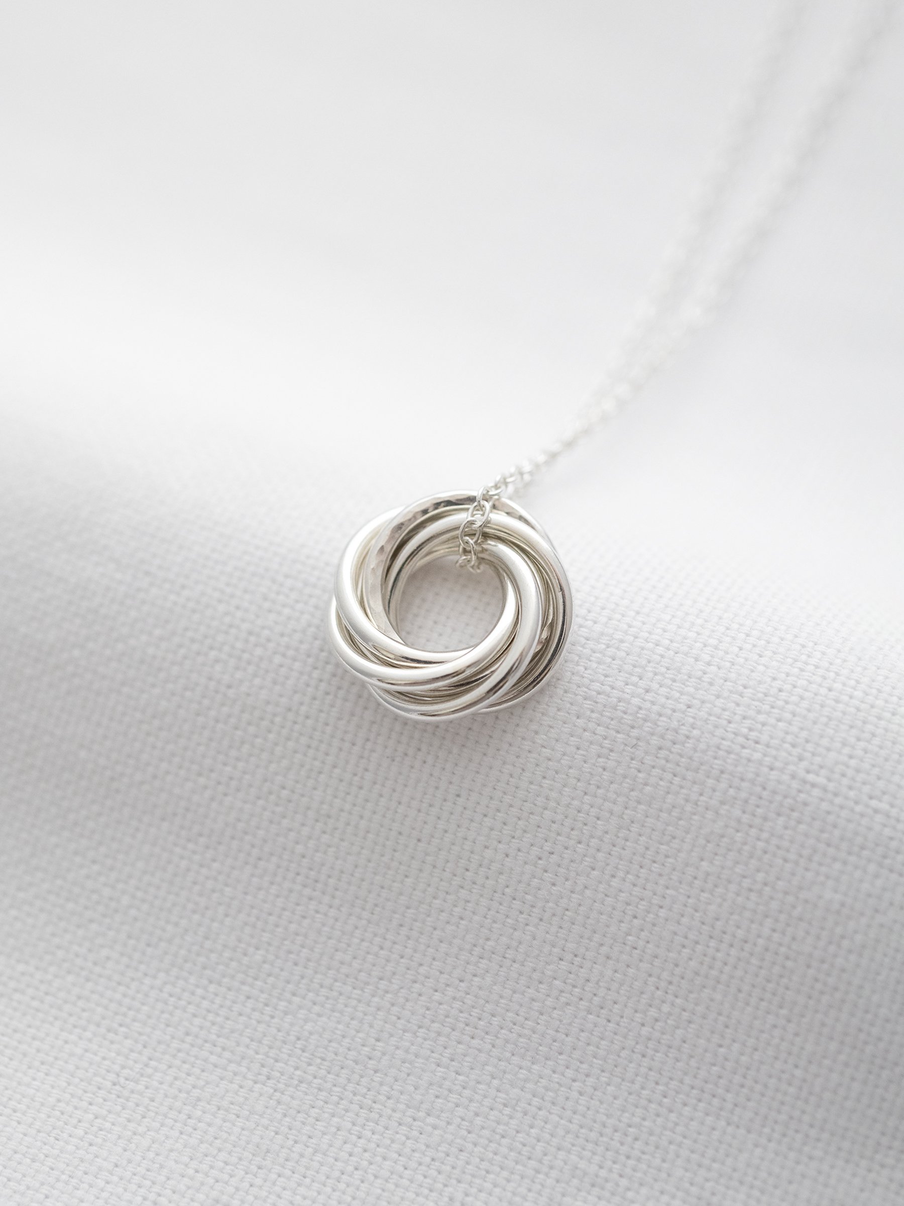 A side view of a silver 60th birthday necklace displayed over white material.