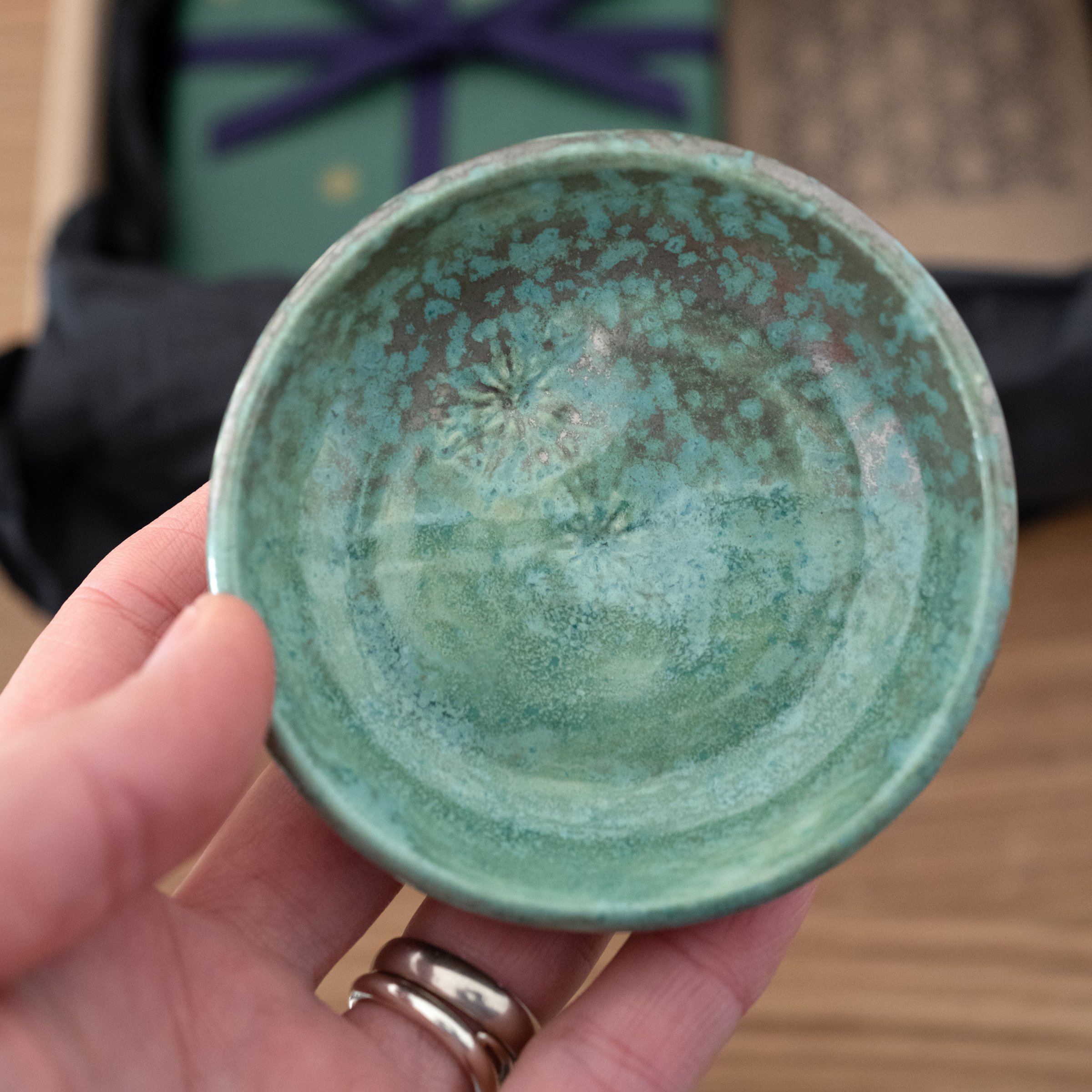 A close up of a person holding a green jewellery dish with jewellery box in the background.