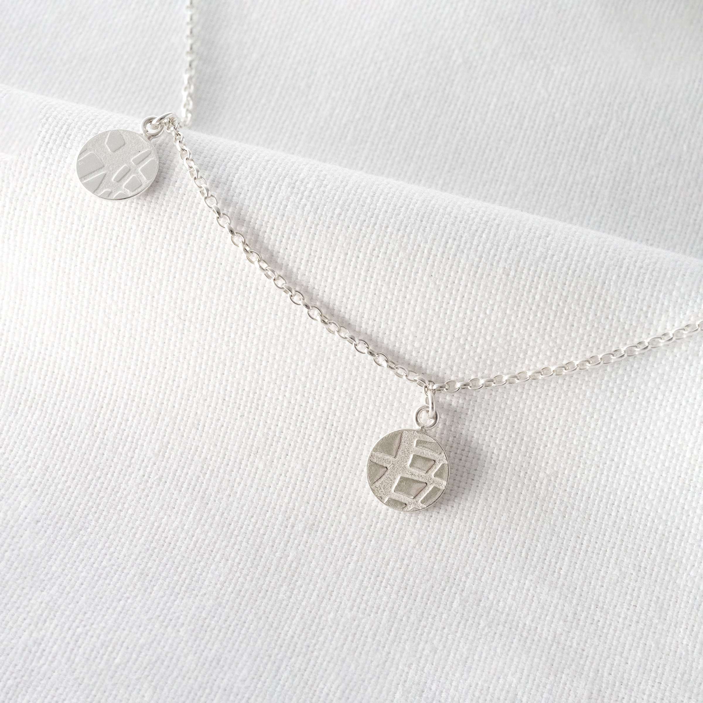 A close up of a silver circle charm necklace hanging over white material.