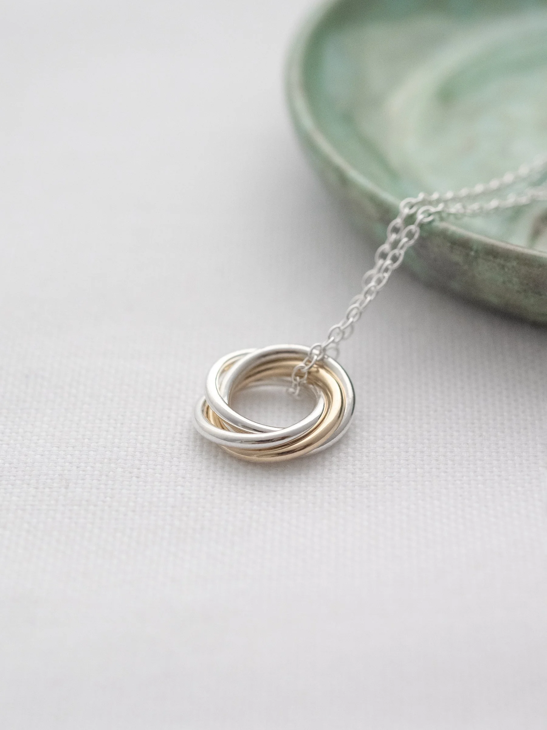 A close up of a 40th gold and silver birthday necklace displayed on white material with a green jewellery dish in the background.