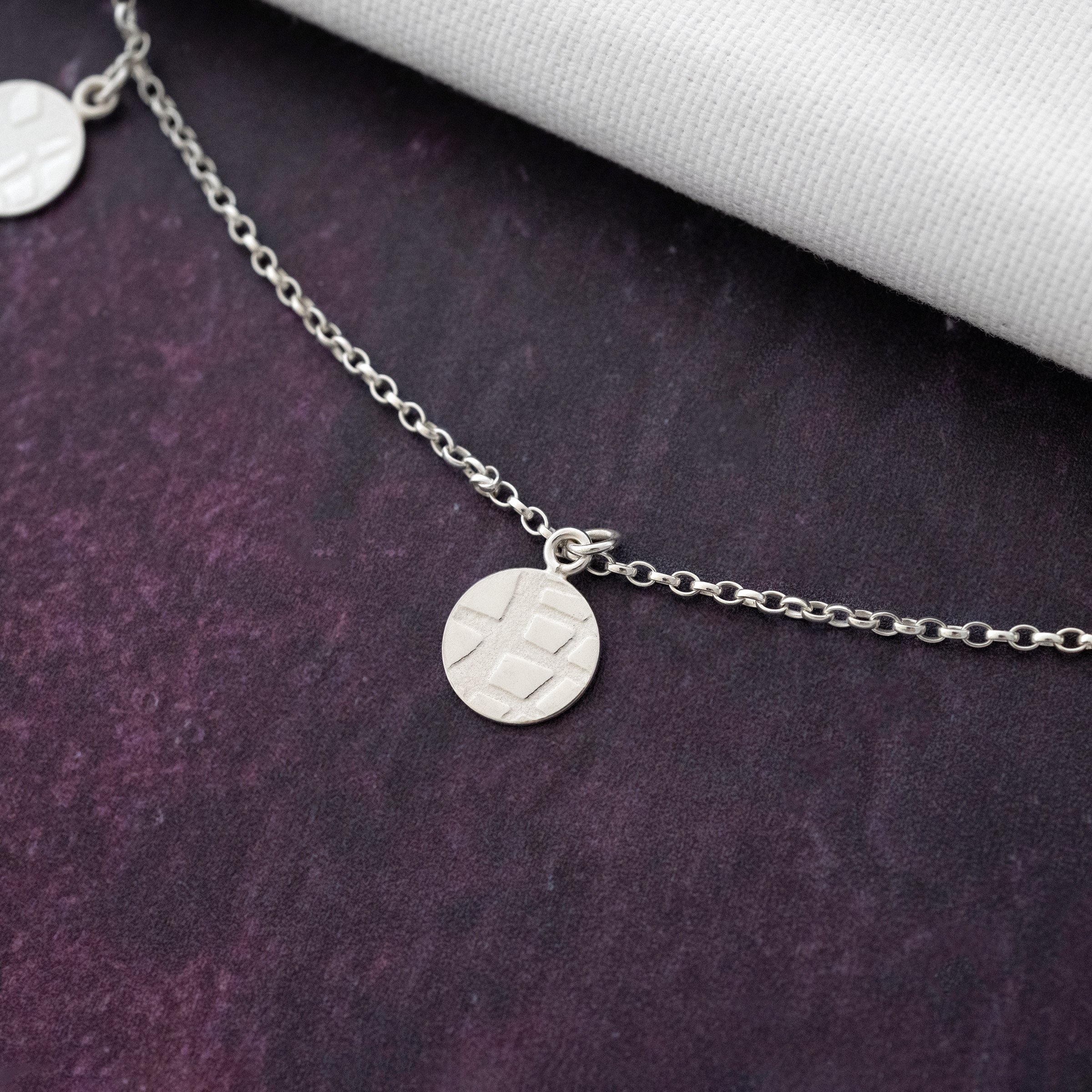 A close up of a silver disc necklace against a purple background.