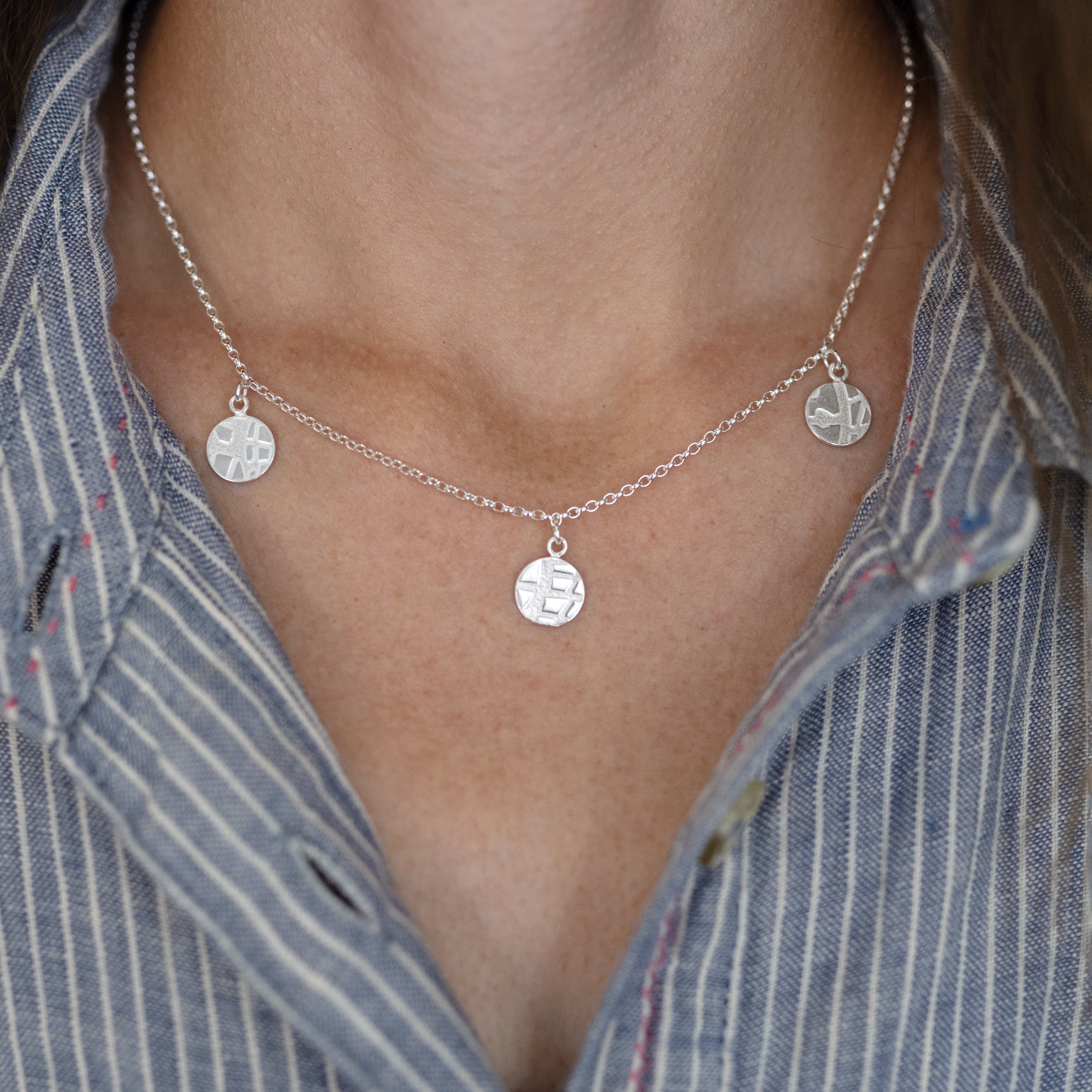 A person wearing a sterling silver circle disc necklace against a blue and white dress.