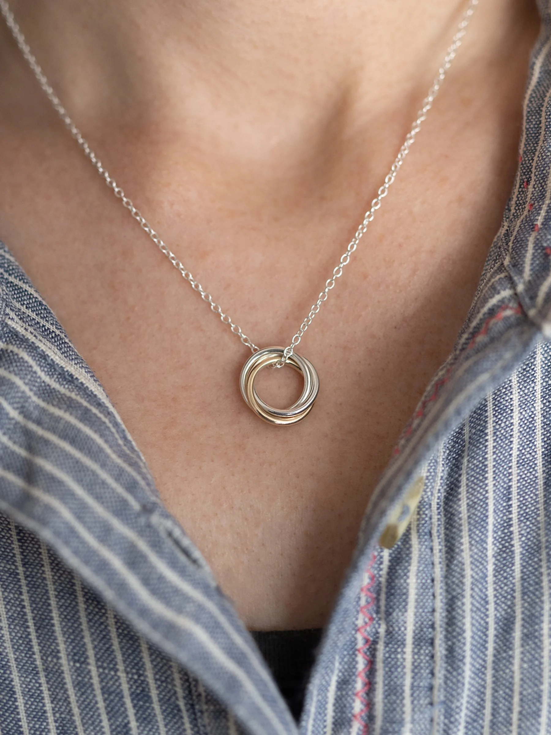 A close up of a person wearing a 30th gold and silver birthday necklace against a blue and white striped dress.
