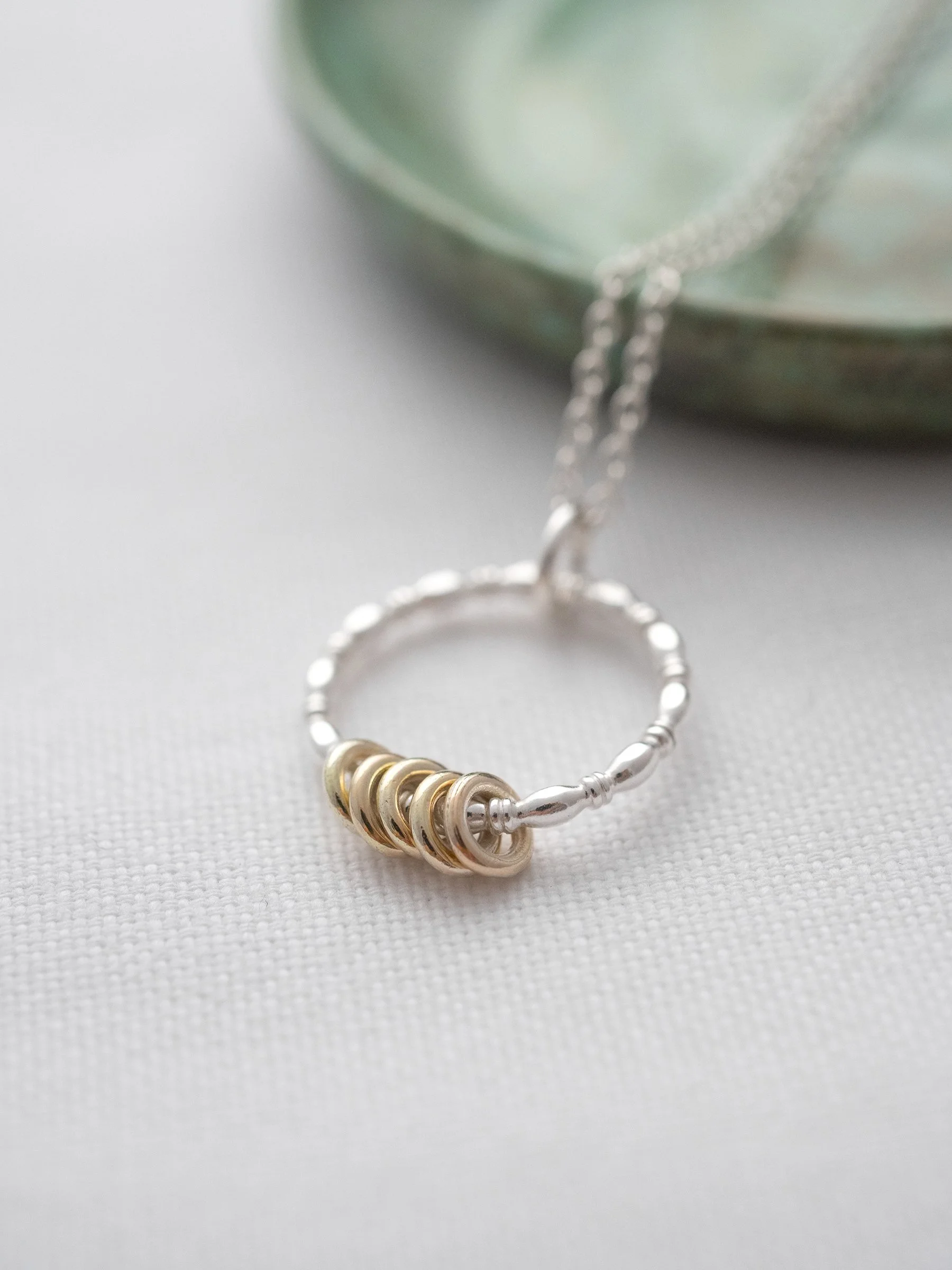 A close up of a gold and silver 5 ring necklace displayed on white material.