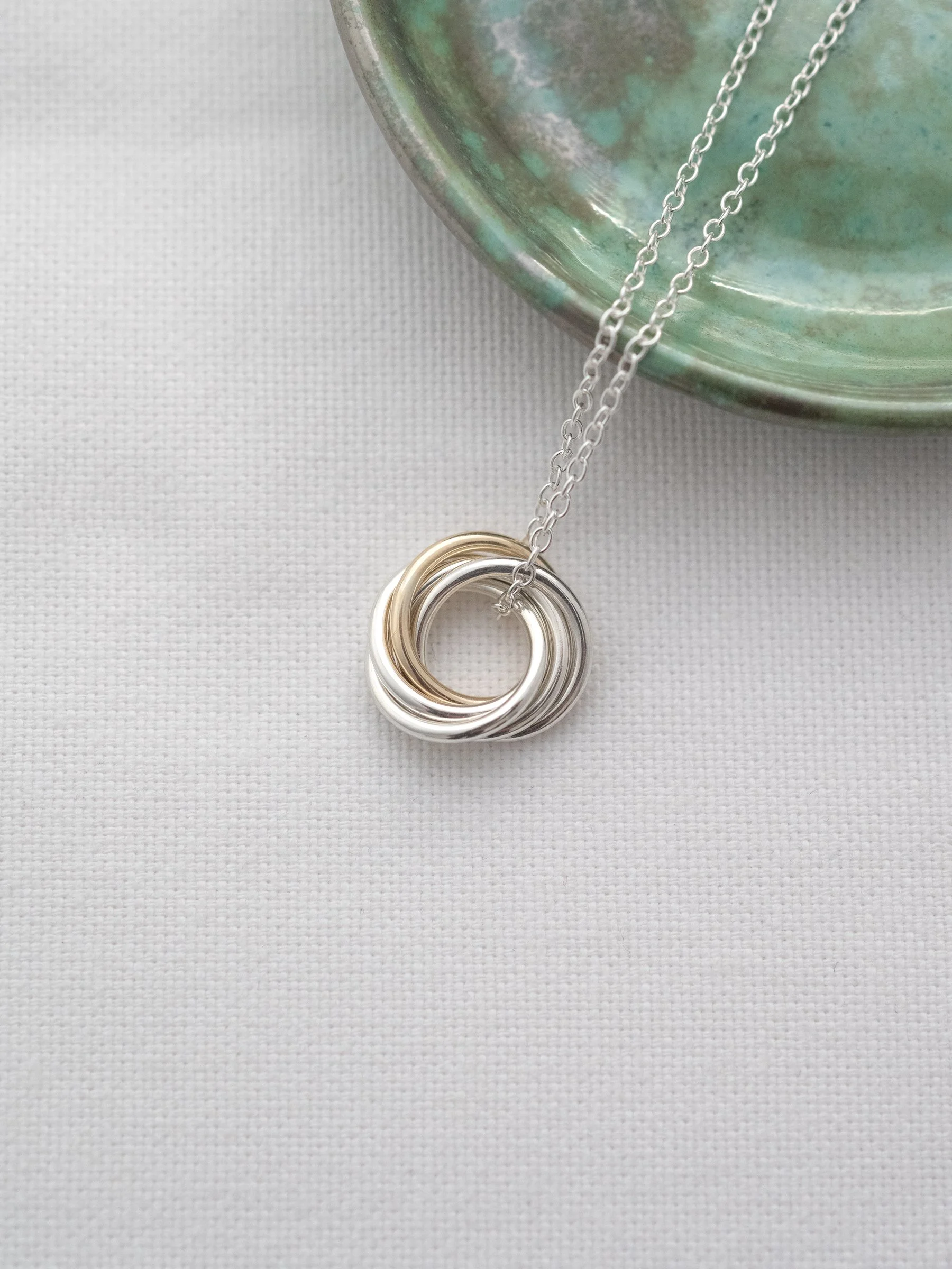 A gold and silver five ring necklace for a 50th birthday displayed on white material with a green jewellery dish in the background.
