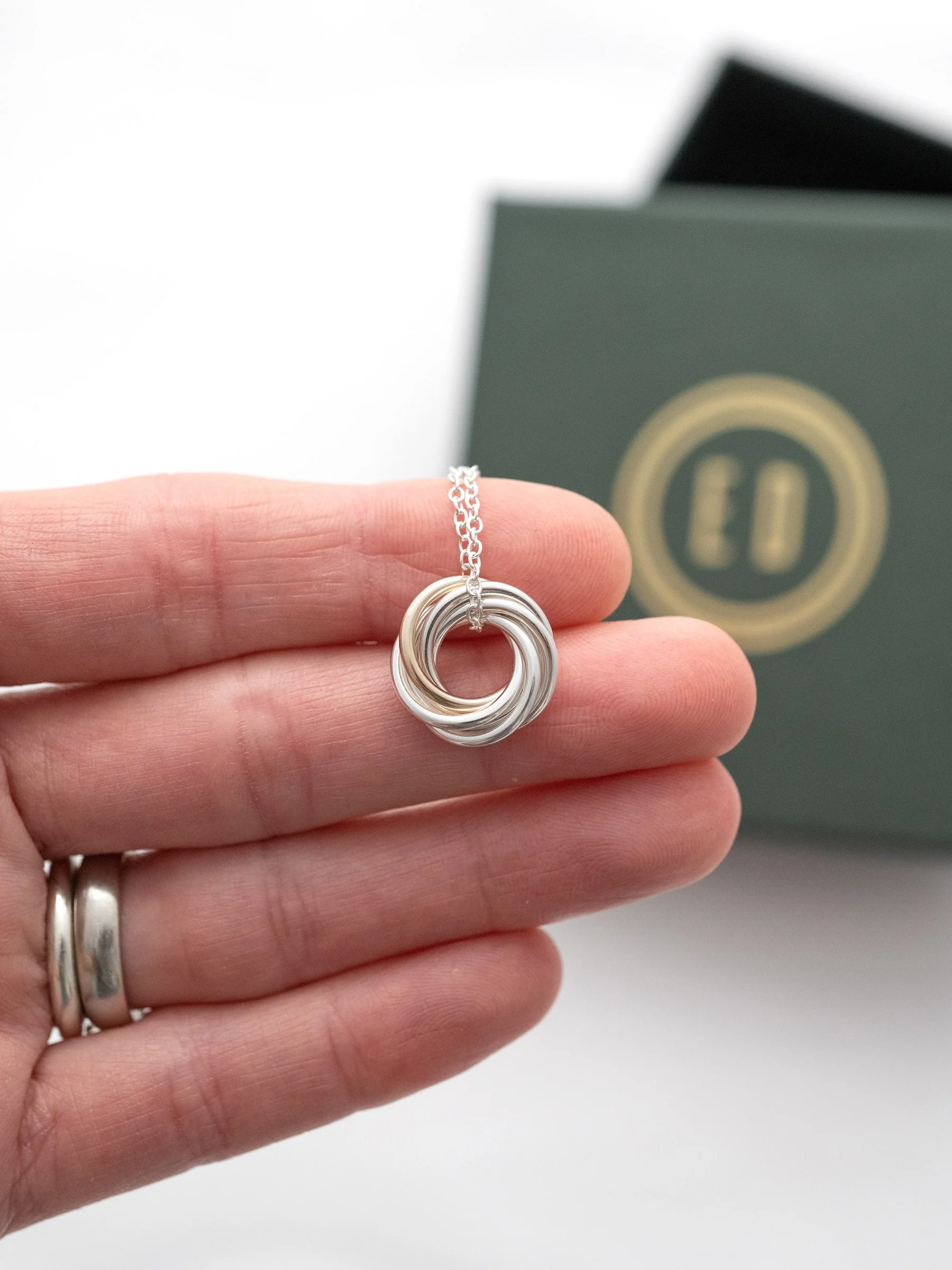 A person displaying a gold and silver 60th birthday necklace in their hand with the presentation box in the background.