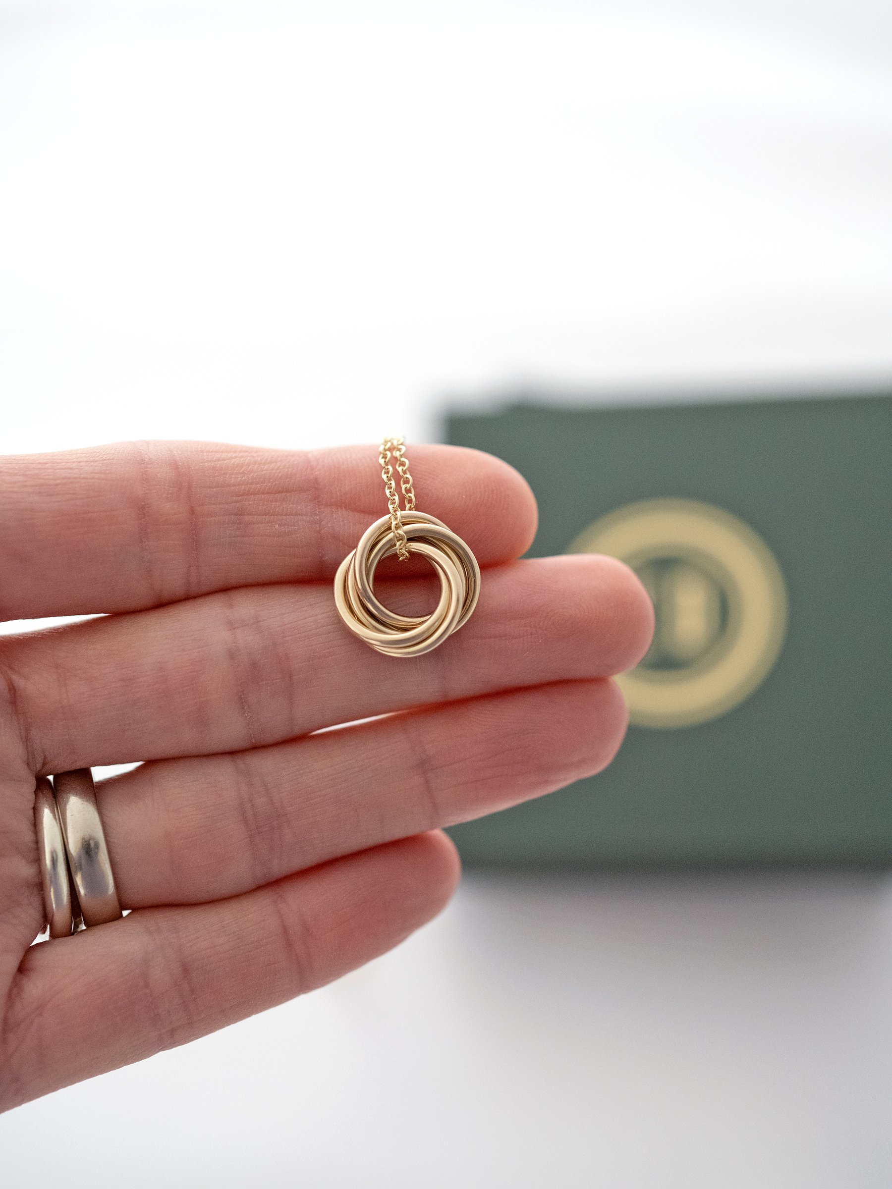 A gold 50th birthday necklace displayed over a persons hand with the presentation box in the background.