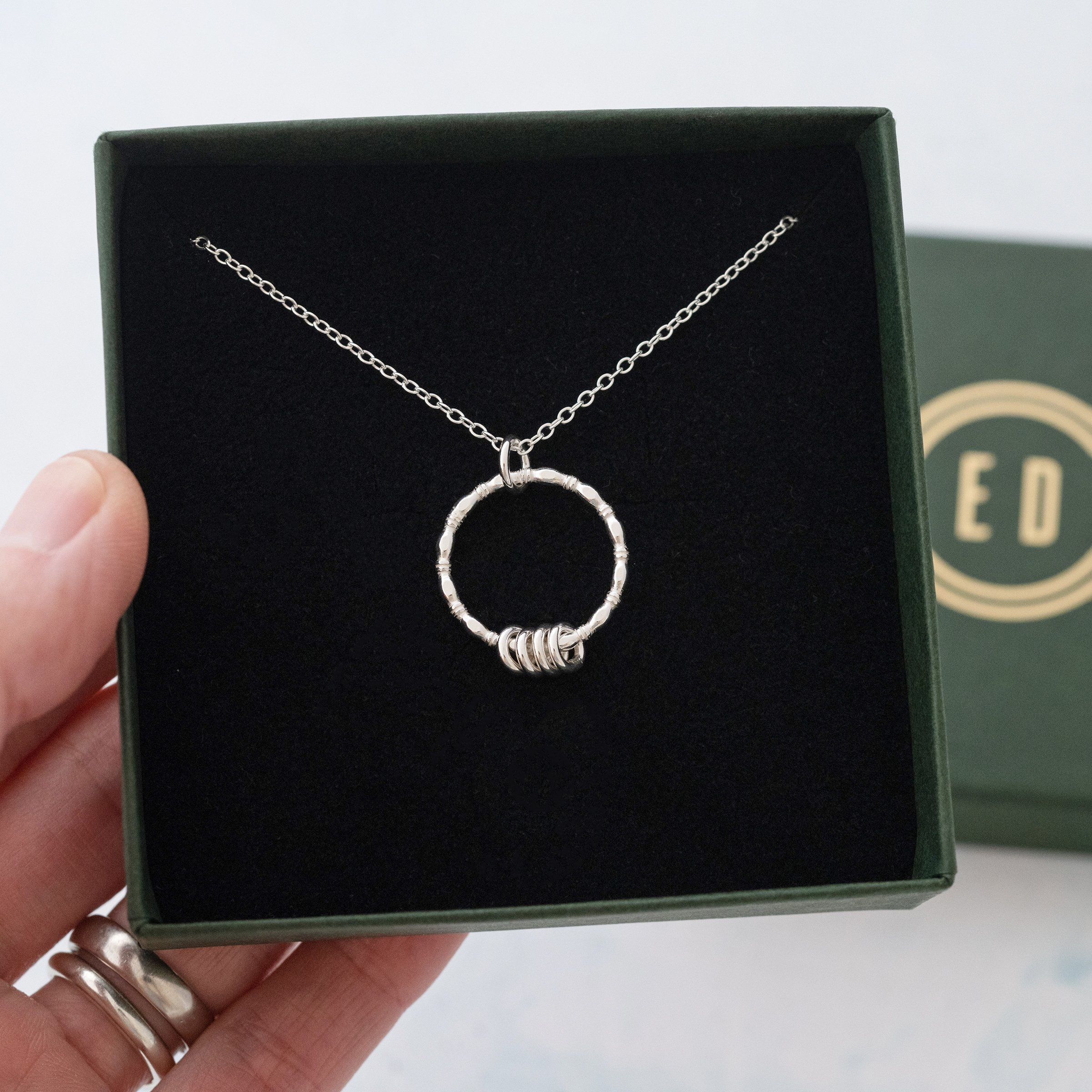 A silver ring necklace displayed in the presentation box.