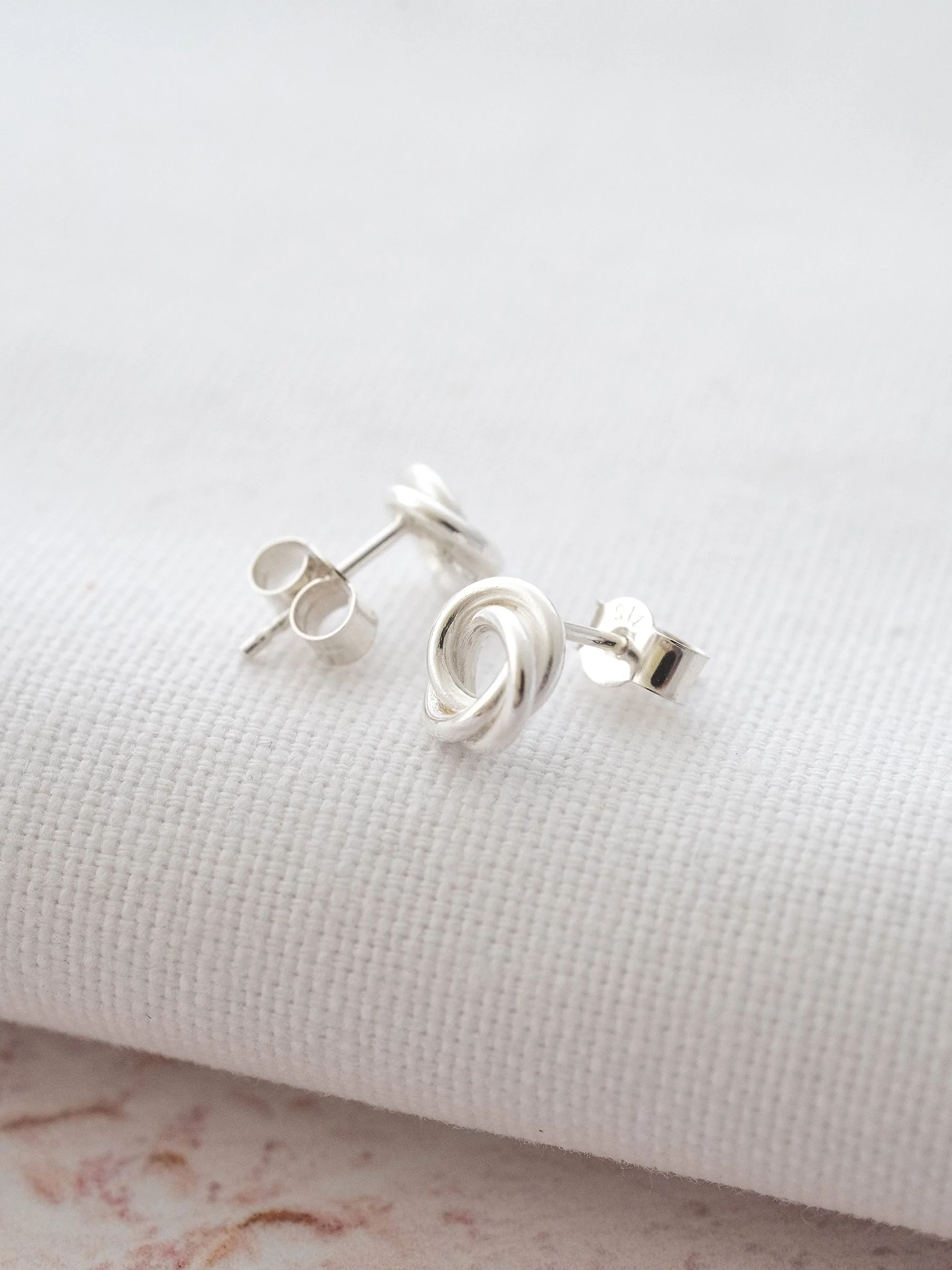 A front a back view of sterling silver Russian ring stud earrings displayed over white material against a pale pink background.