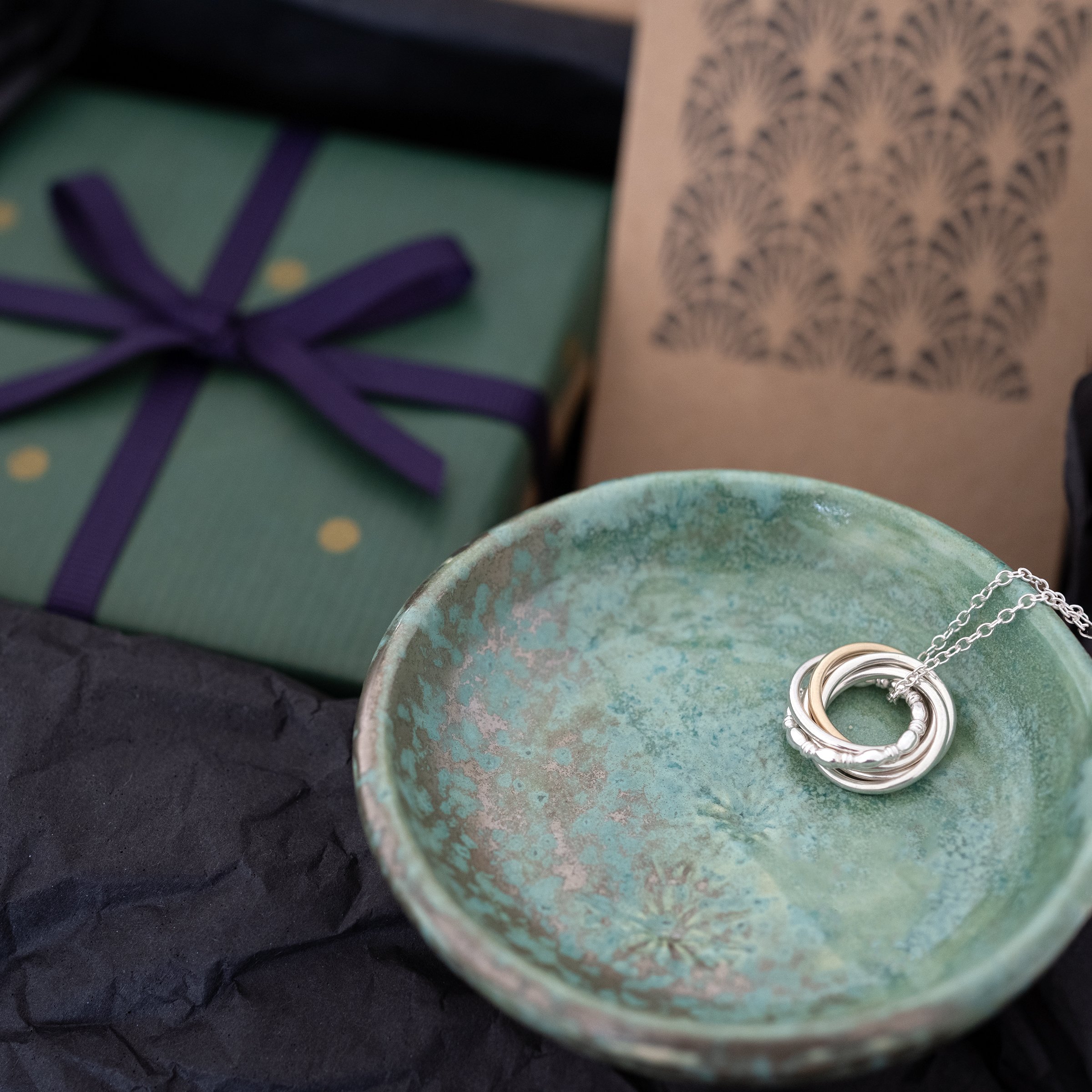 A close up of a green jewellery dish with jewellery gift box in the background.