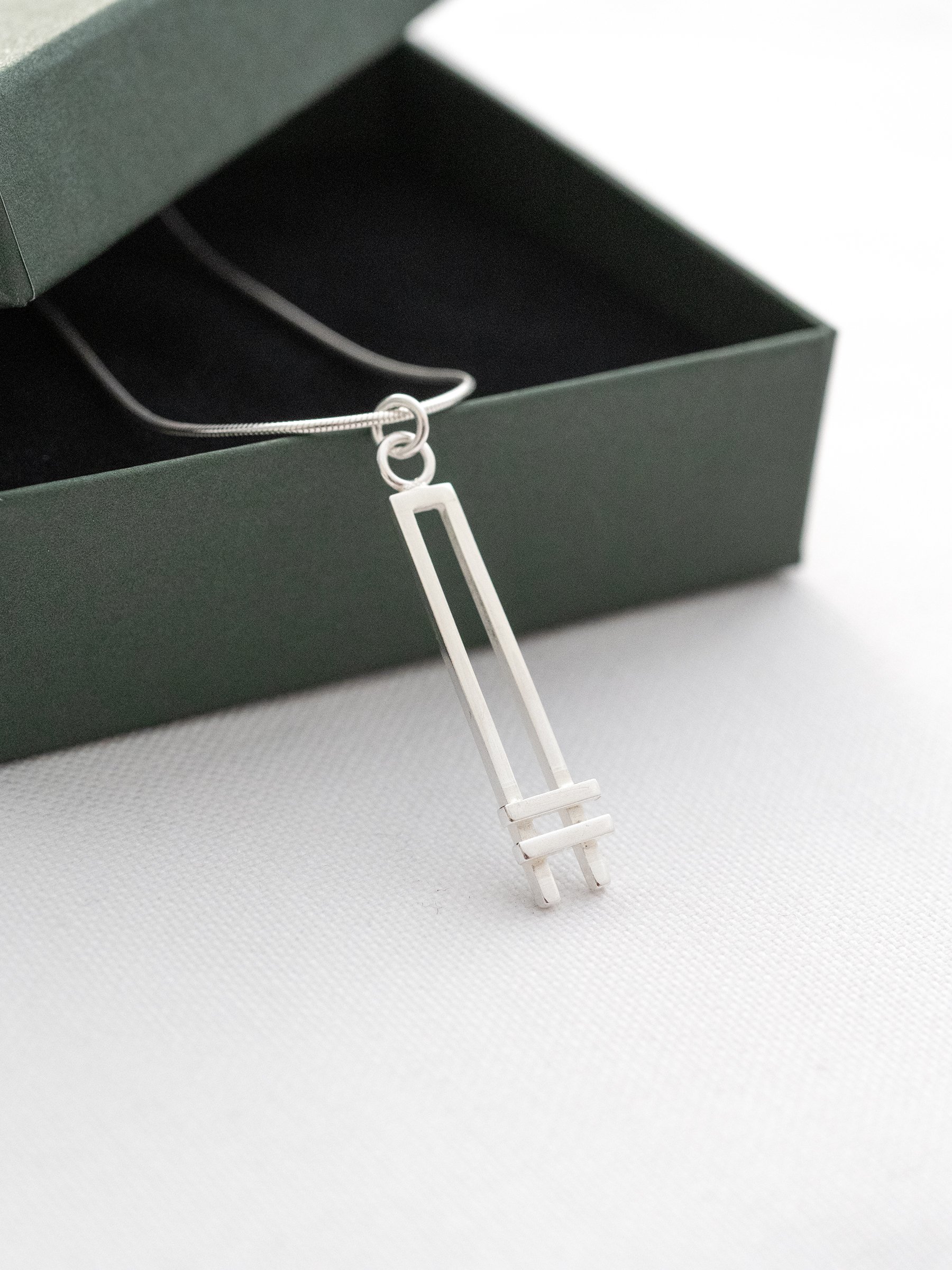 A side view of a sterling silver Art Deco style necklace resting against a green jewellery presentation box.