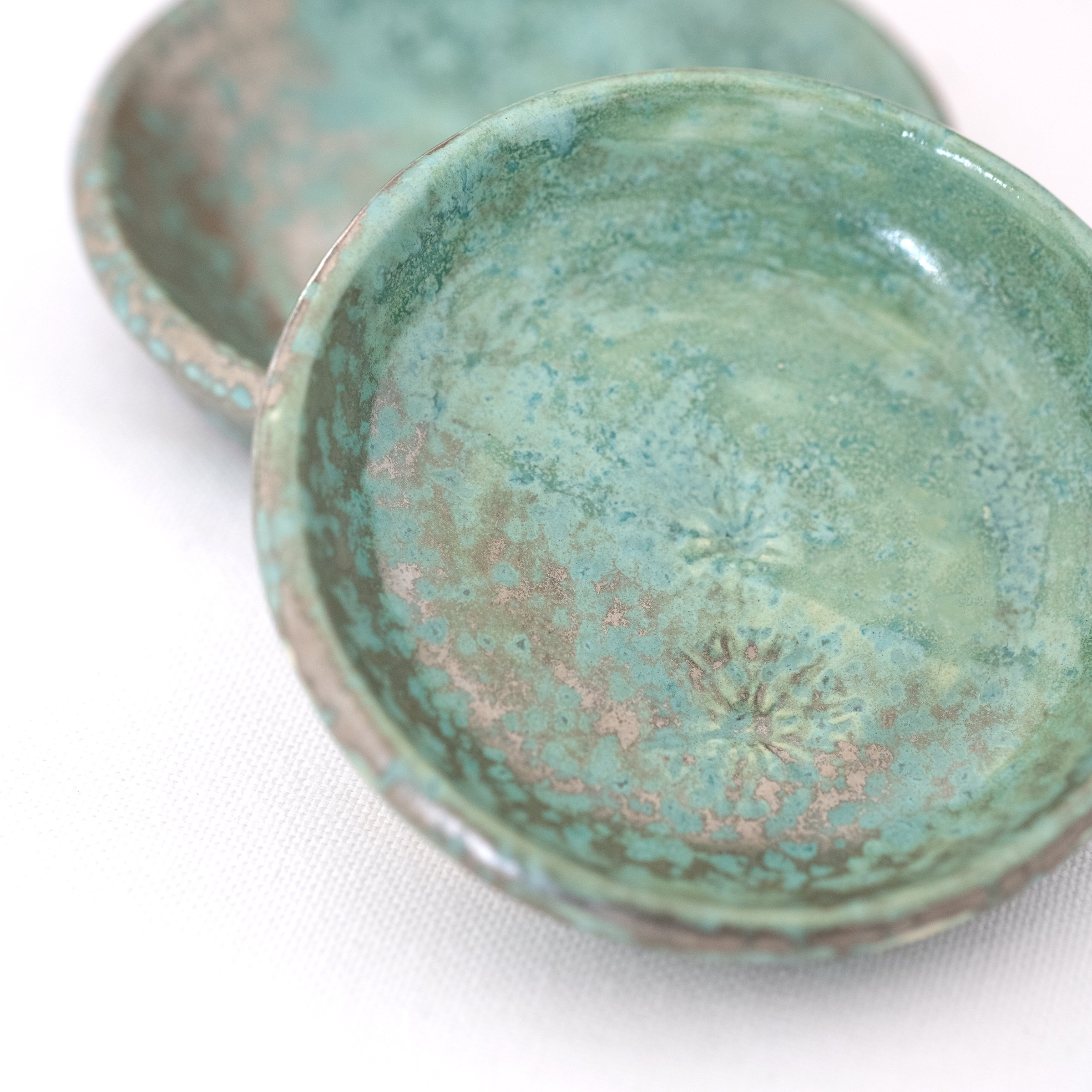 A close up of two green jewellery dishes next to each other against a white background.