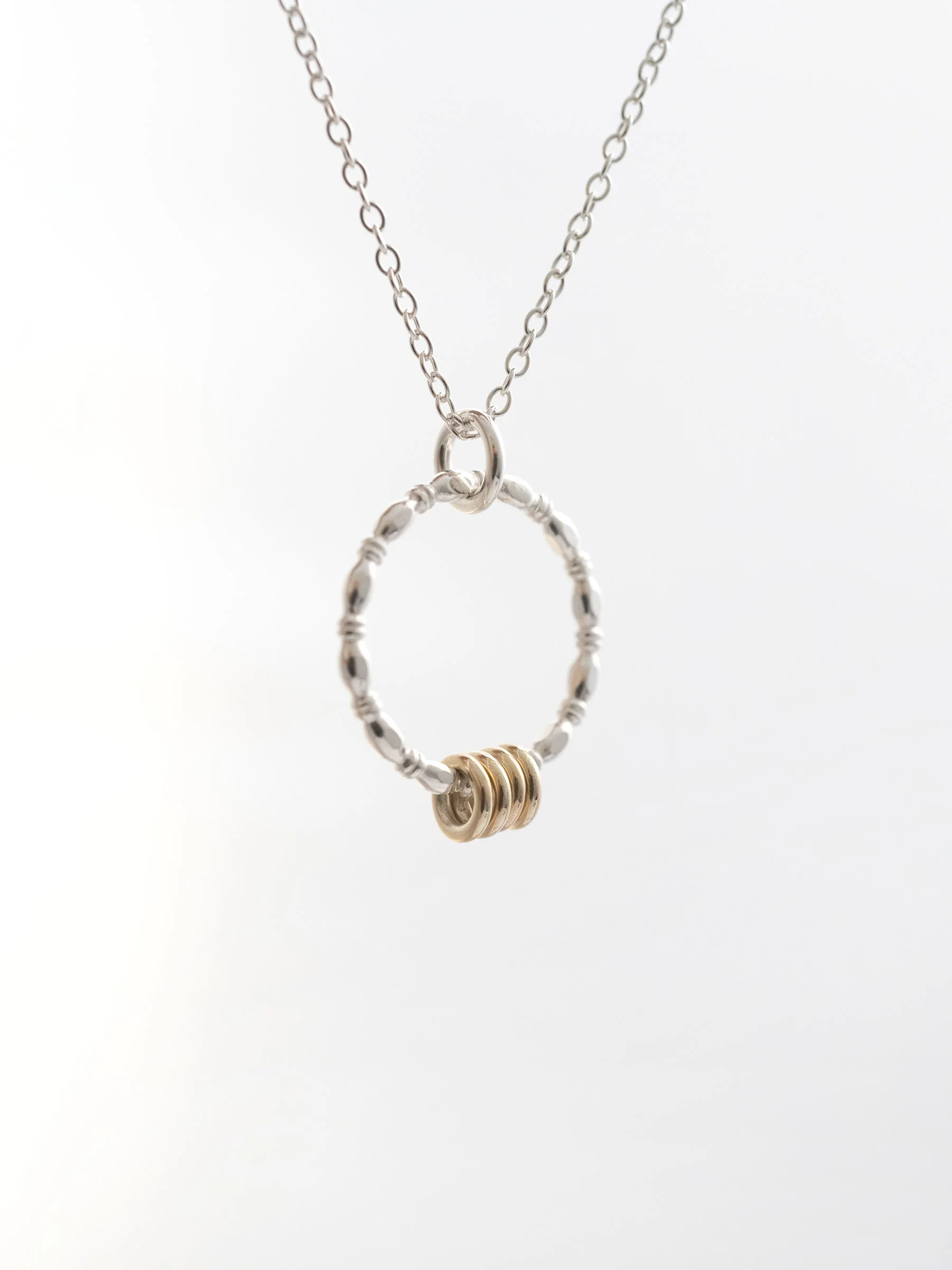 A unique gold and silver four ring necklace hanging against a light grey background.