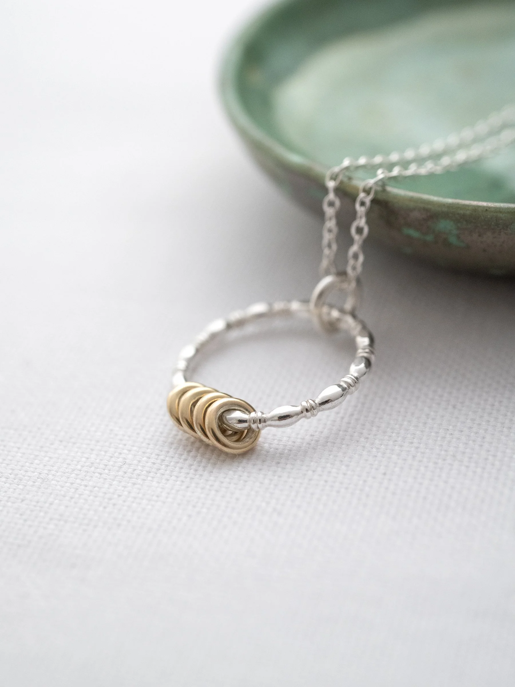 A close up of a gold and silver 40th ring necklace displayed next to a green jewellery dish.