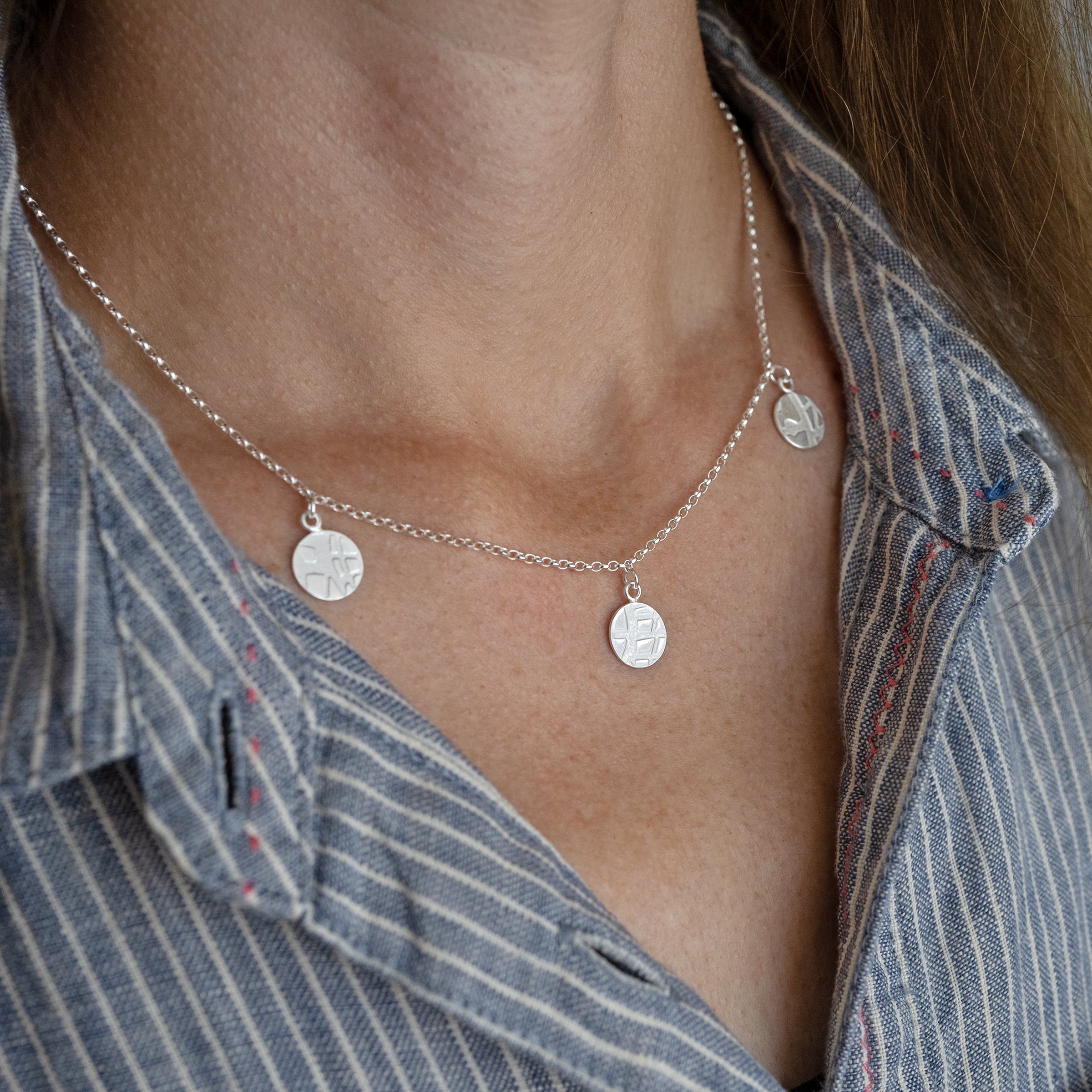 A side view of a person wearing a silver circle textured necklace against a blue and white dress.