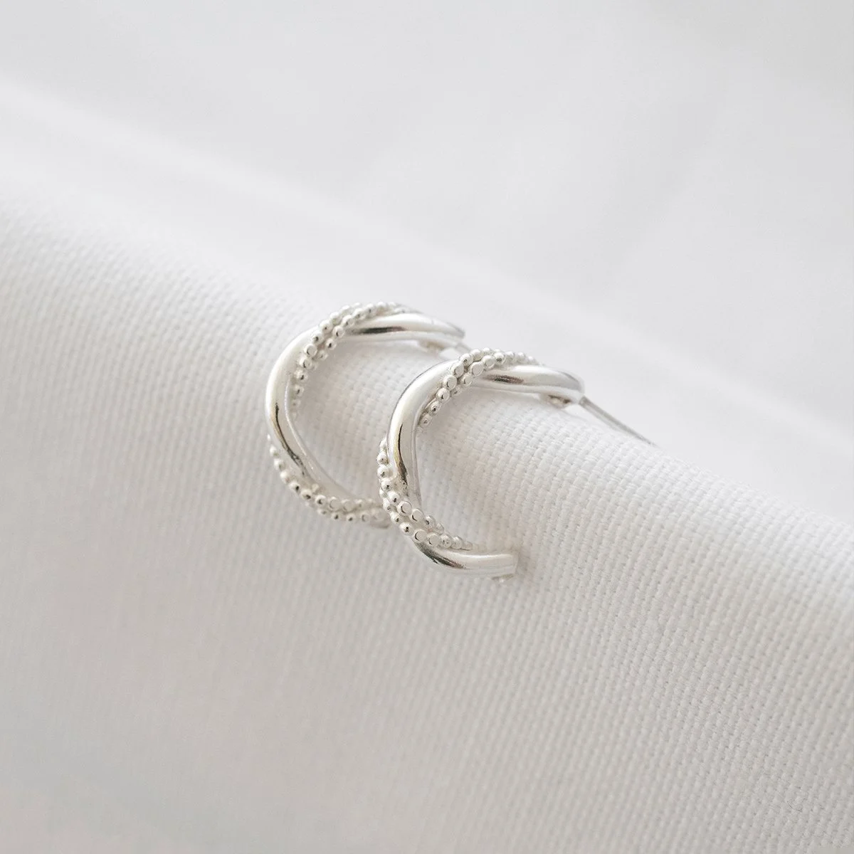 A pair of unique sterling silver half hoop earrings displayed on white material.