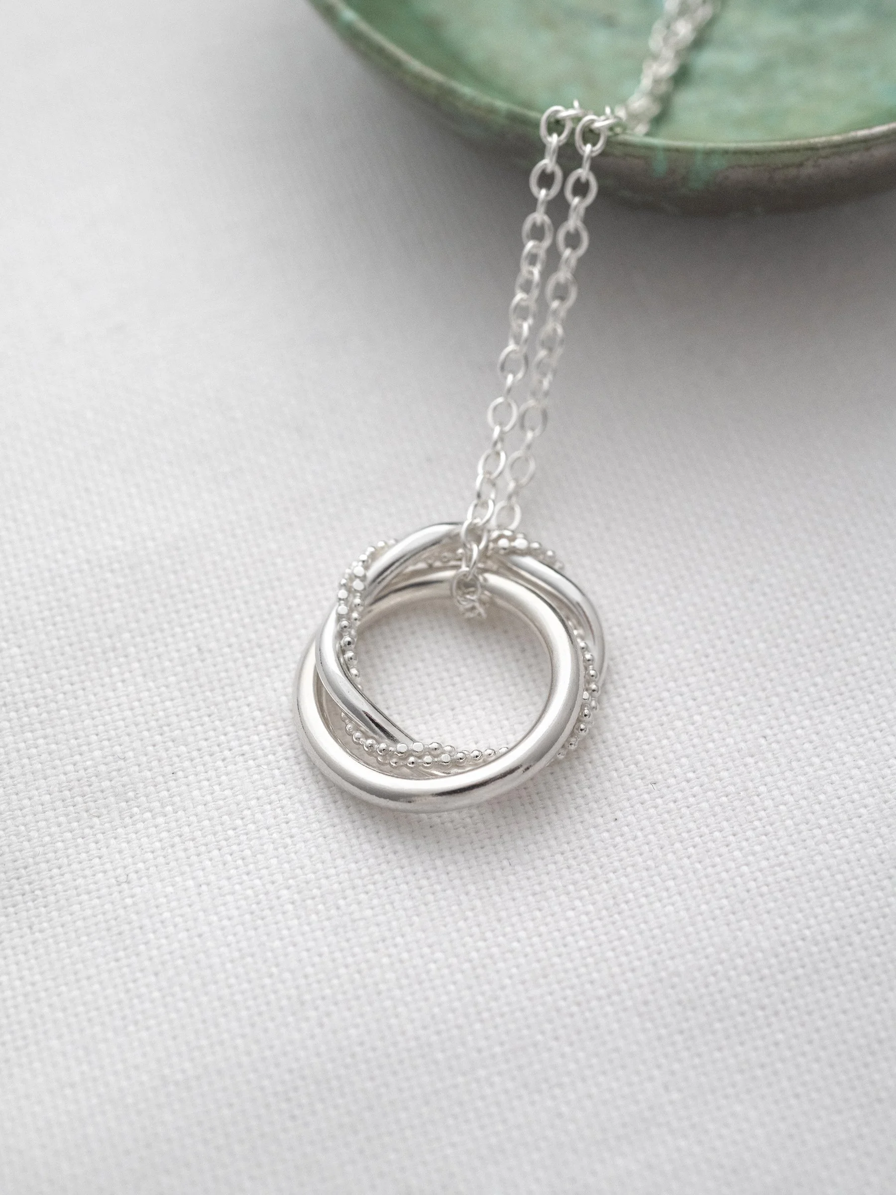 A unique 21st birthday necklace displayed on white material with a green jewellery dish in the background.