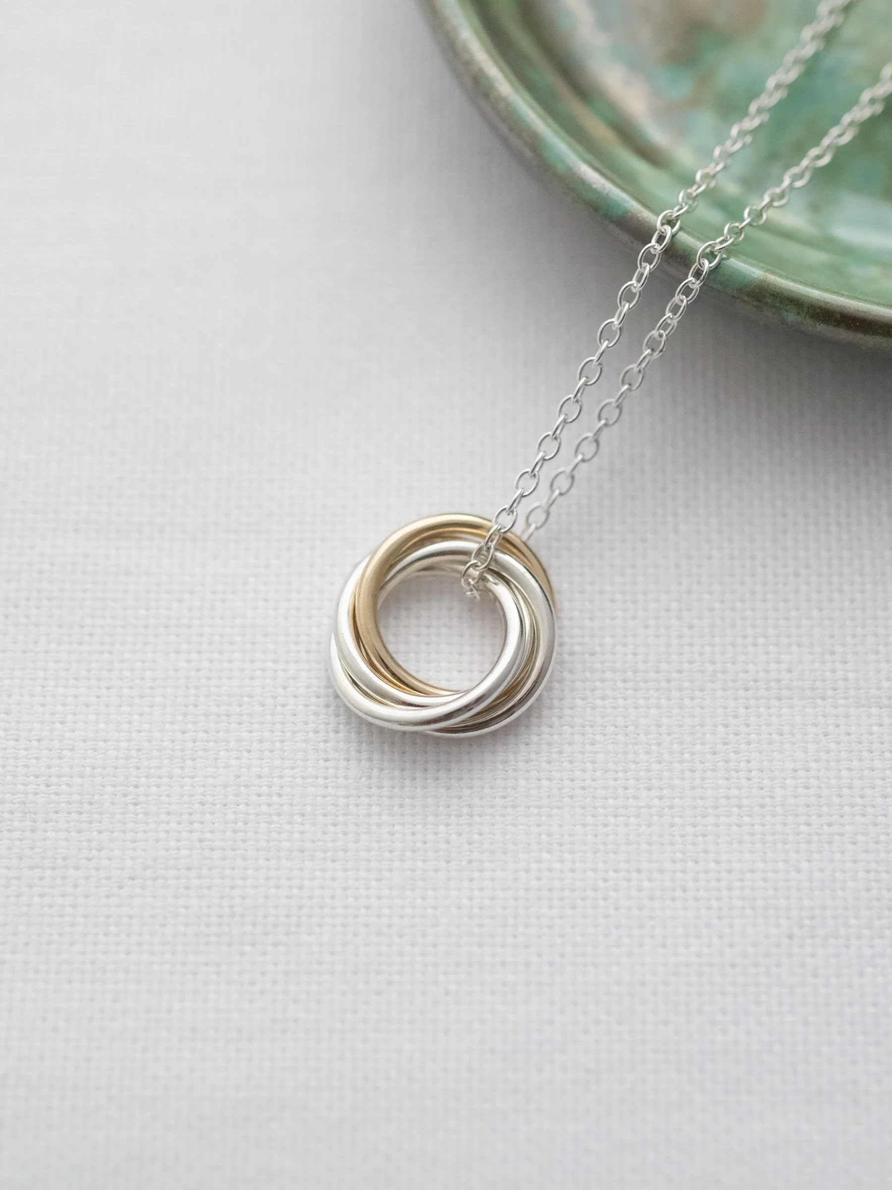A unique gold and silver necklace for a 40th birthday displayed on white material with a green jewellery dish in the background.