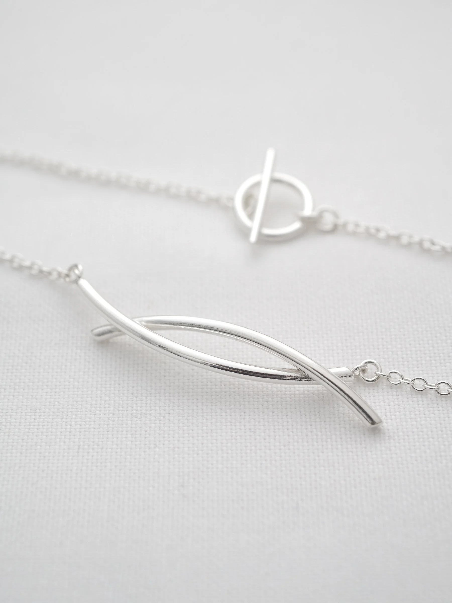 A close up of a sterling silver entwined twist necklace displayed on white material.