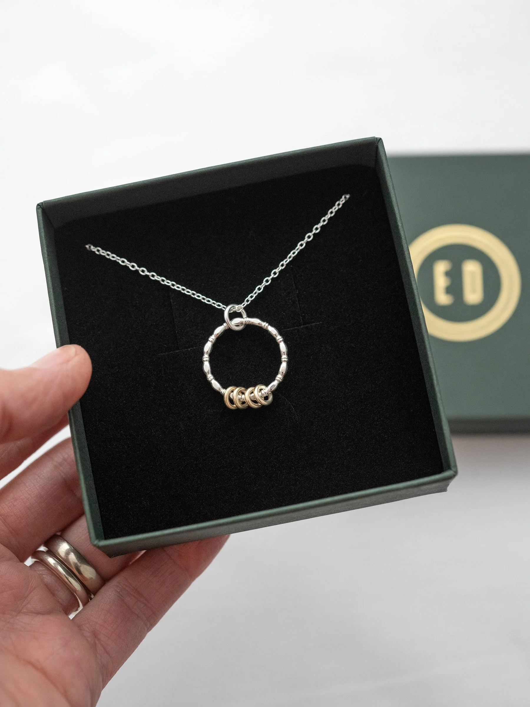 A gold and silver four ring necklace displayed in an jewellery presentation box.