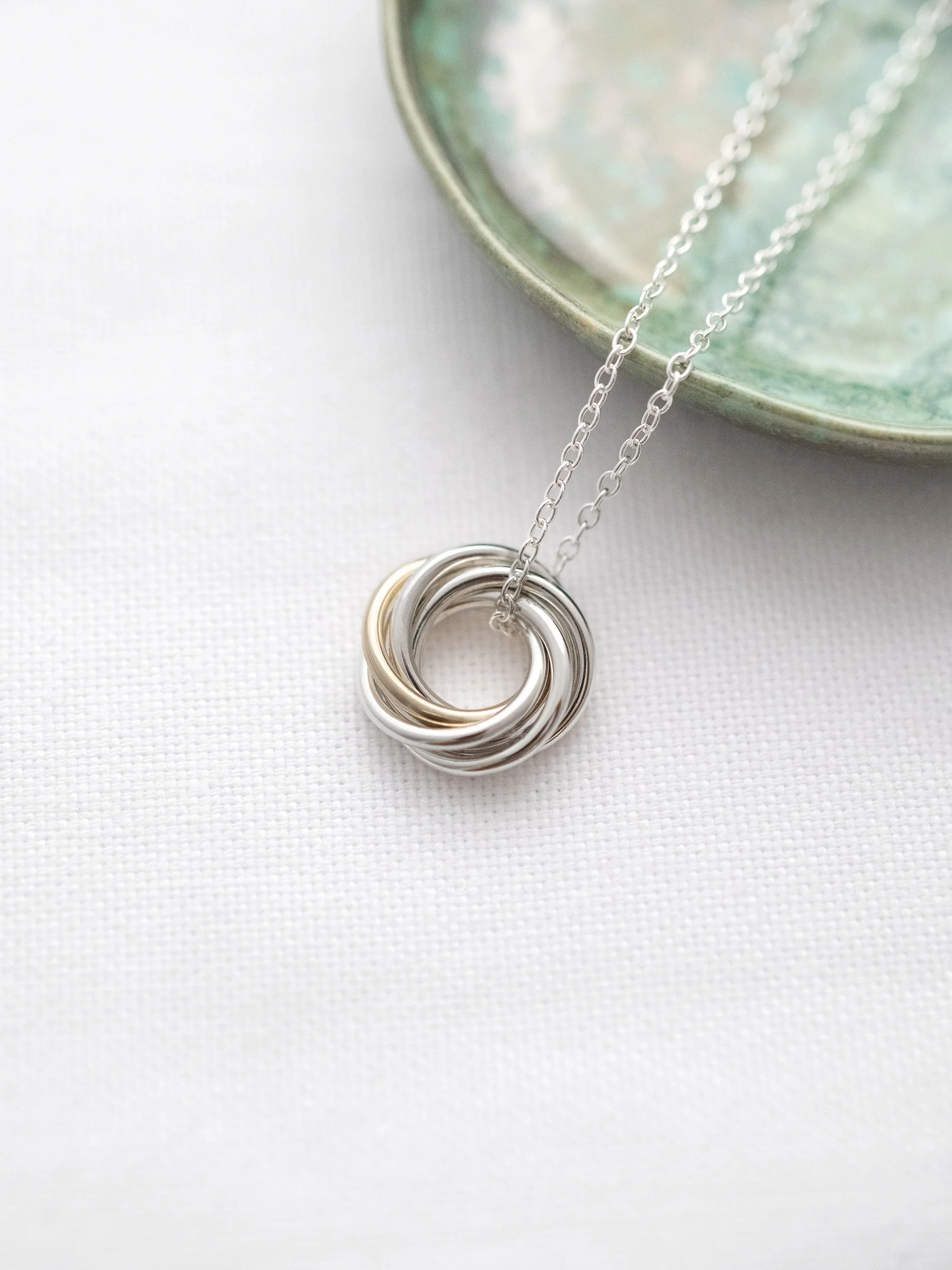 A 9 carat gold and silver 60th birthday necklace displayed on white material with a green jewellery dish in the background.