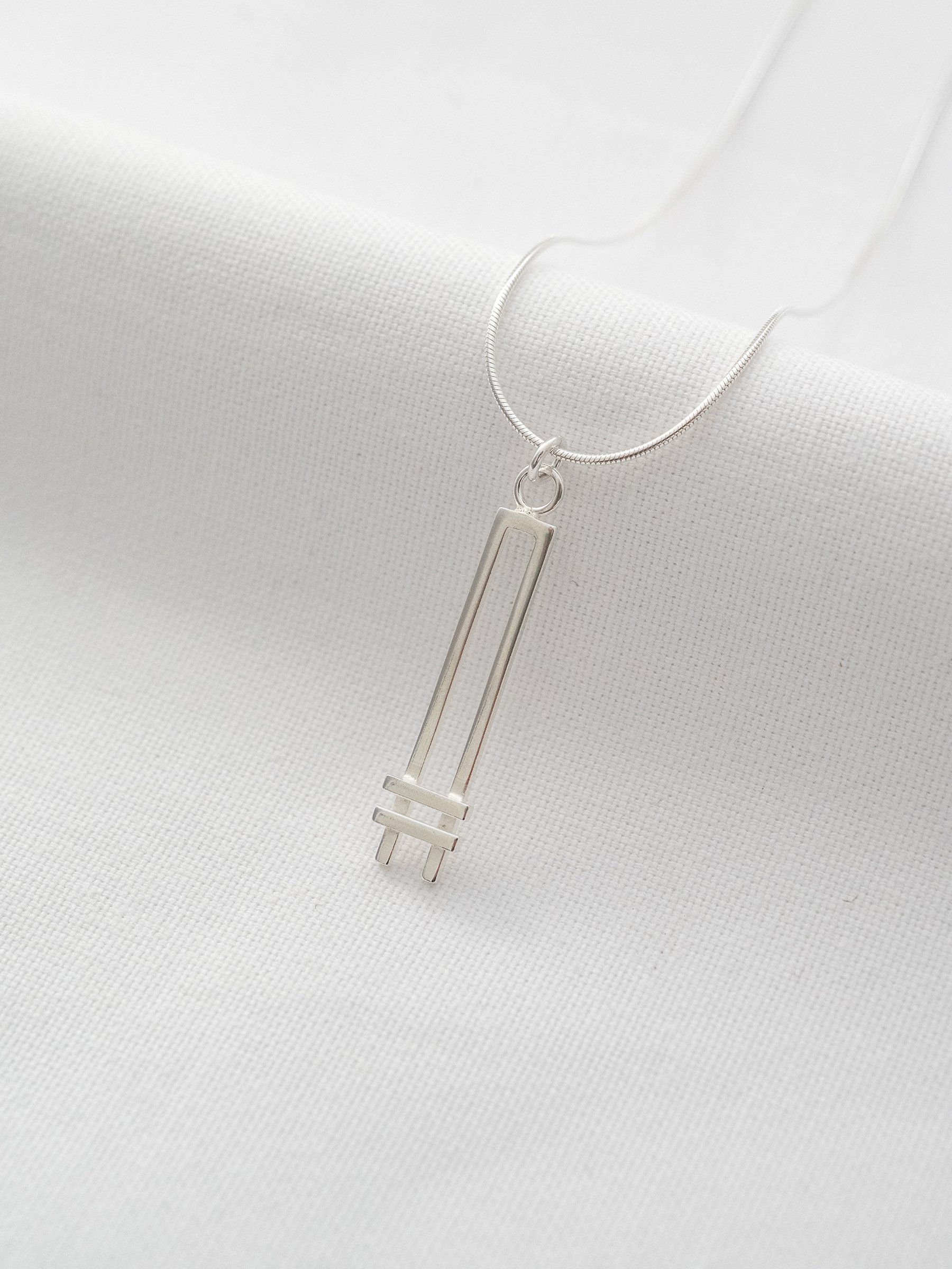 A silver Art Deco style necklace displayed on white material.