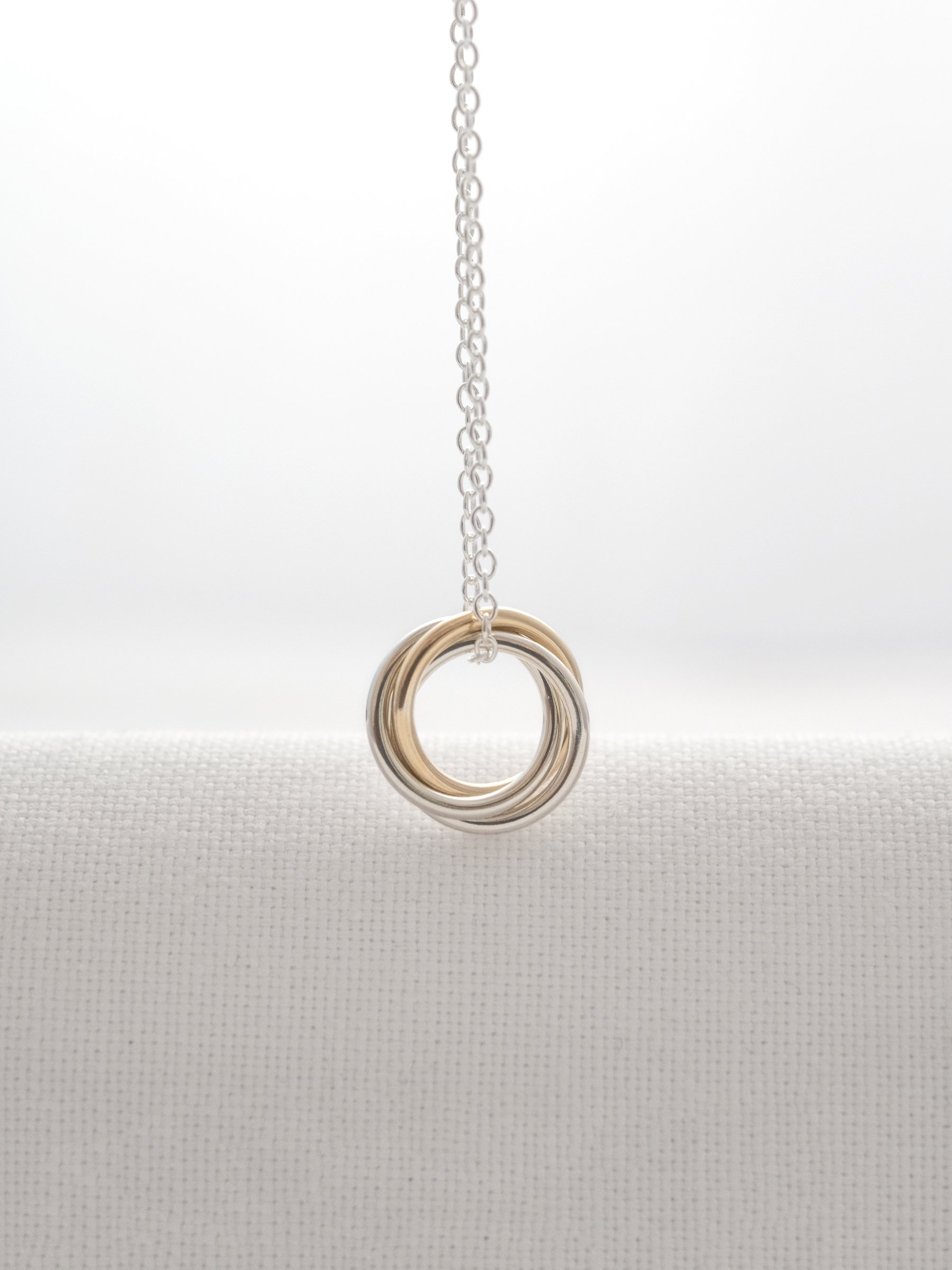 A unique gold and silver 30th necklace hanging over white material.