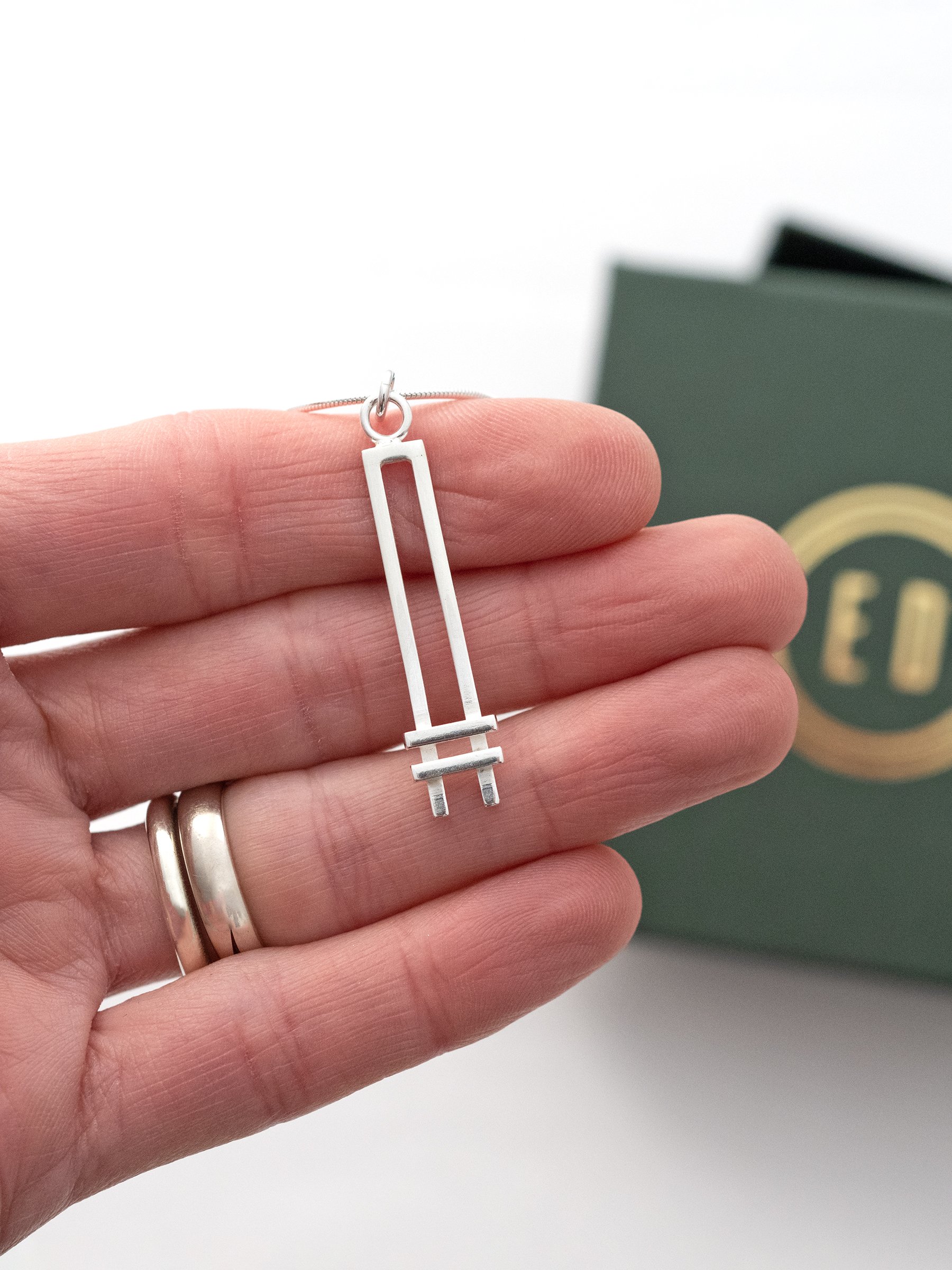 A sterling silver Art Deco style necklace displayed in a persons hand with the presentation box in the background.