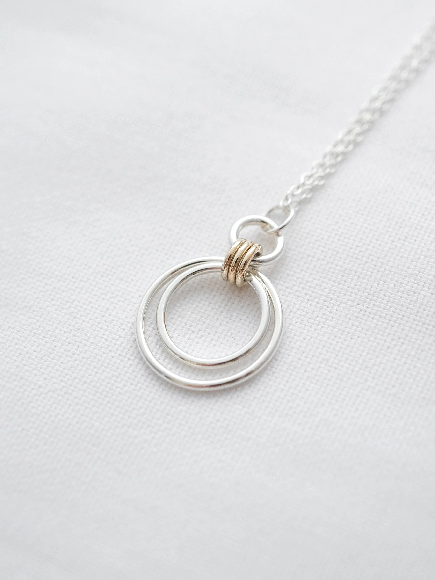 A gold and silver family necklace displayed on white material.