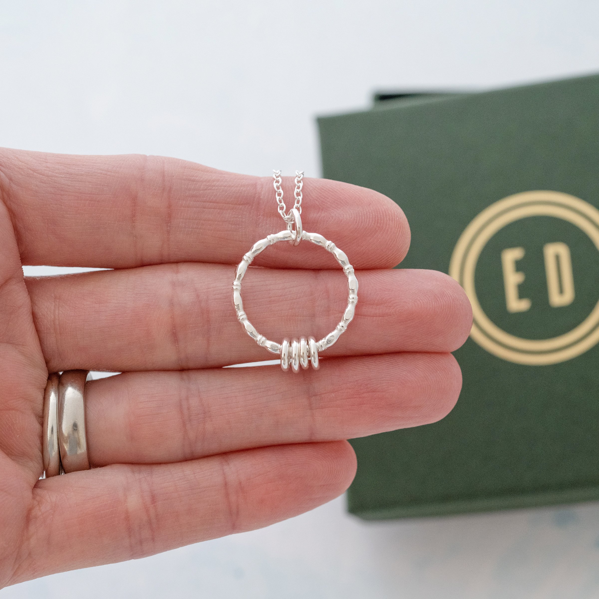 A sterling silver four ring necklace displayed over a persons hand with the green presentation box in the background..