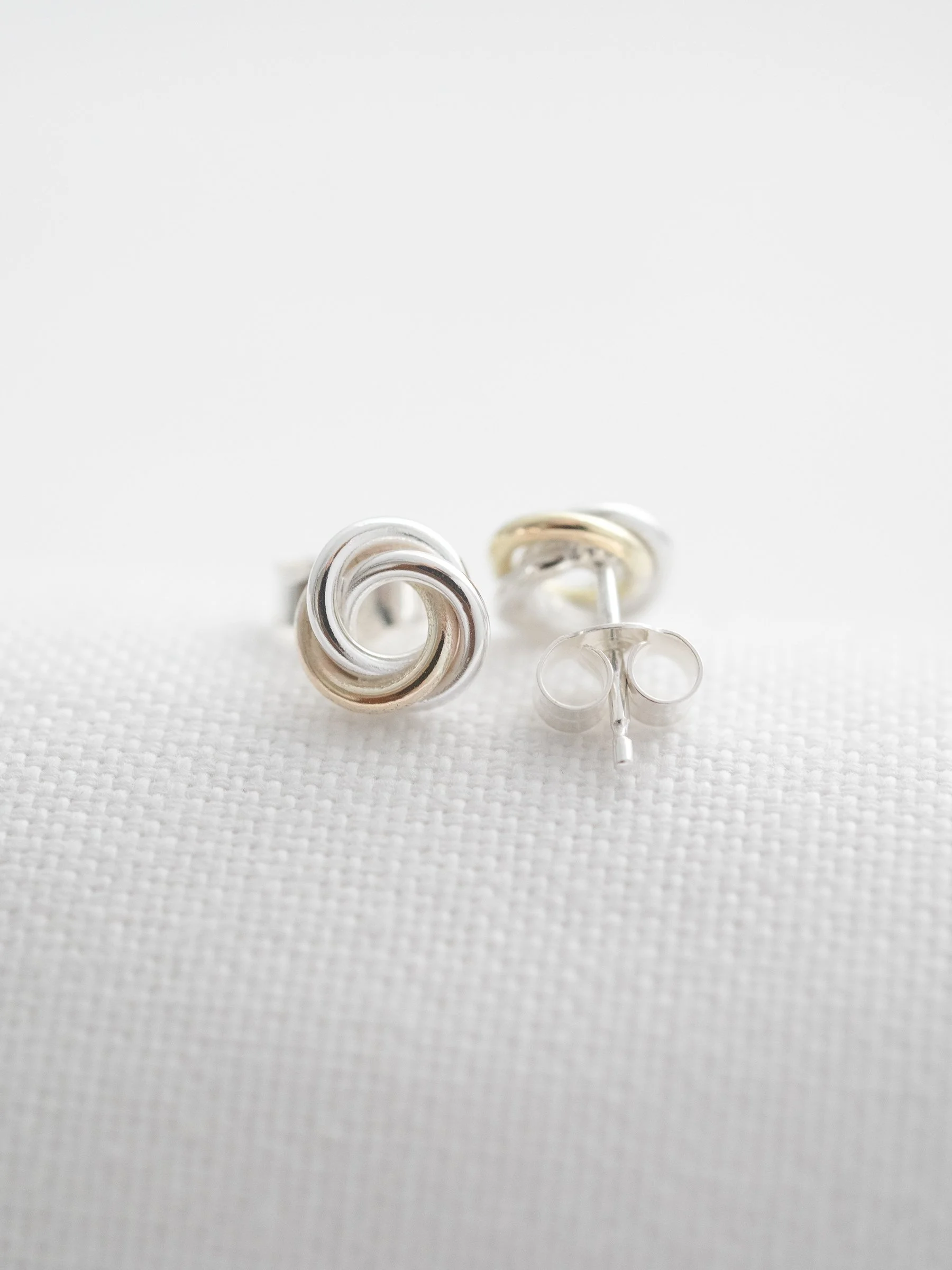 A pair of gold and silver Russian ring stud earrings displayed on white material.