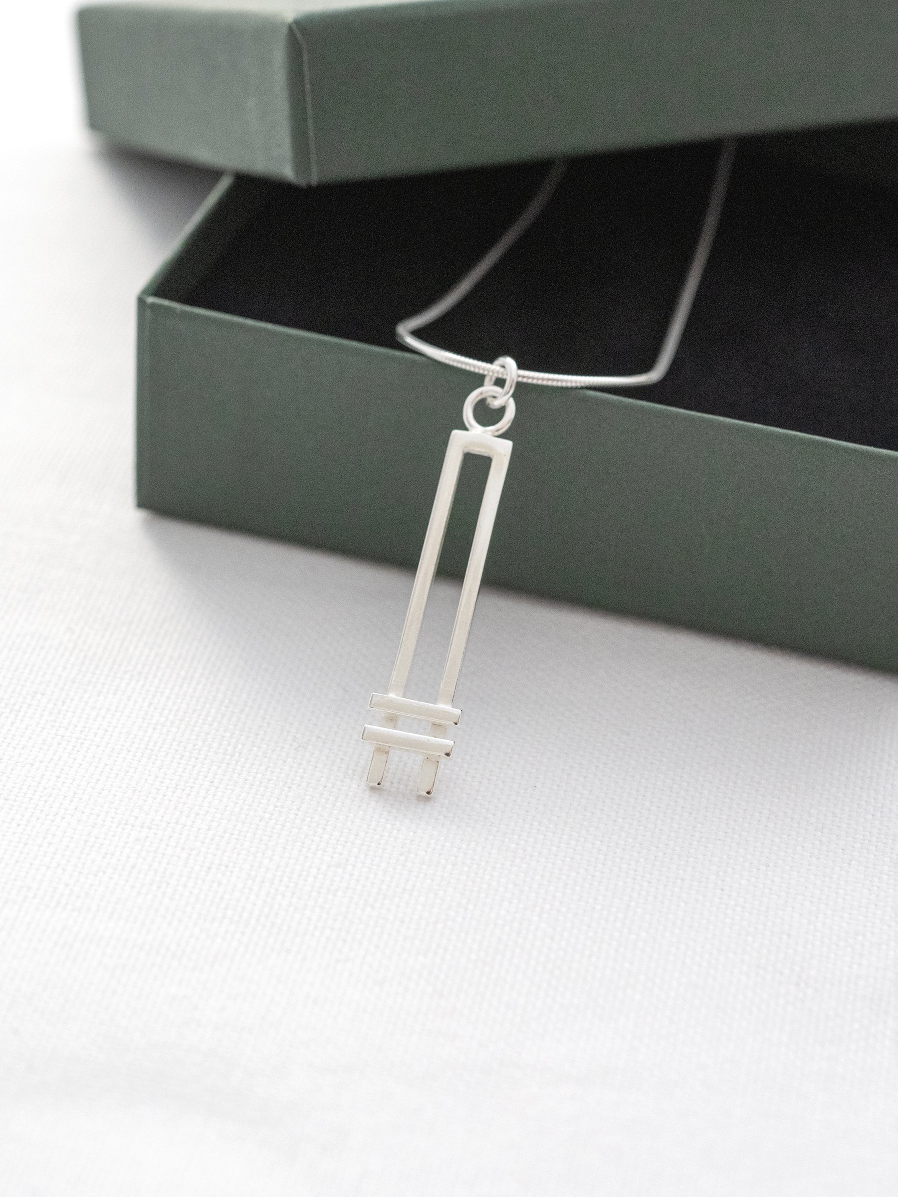 A sterling silver Art Deco style necklace displayed against a green jewellery presentation box.