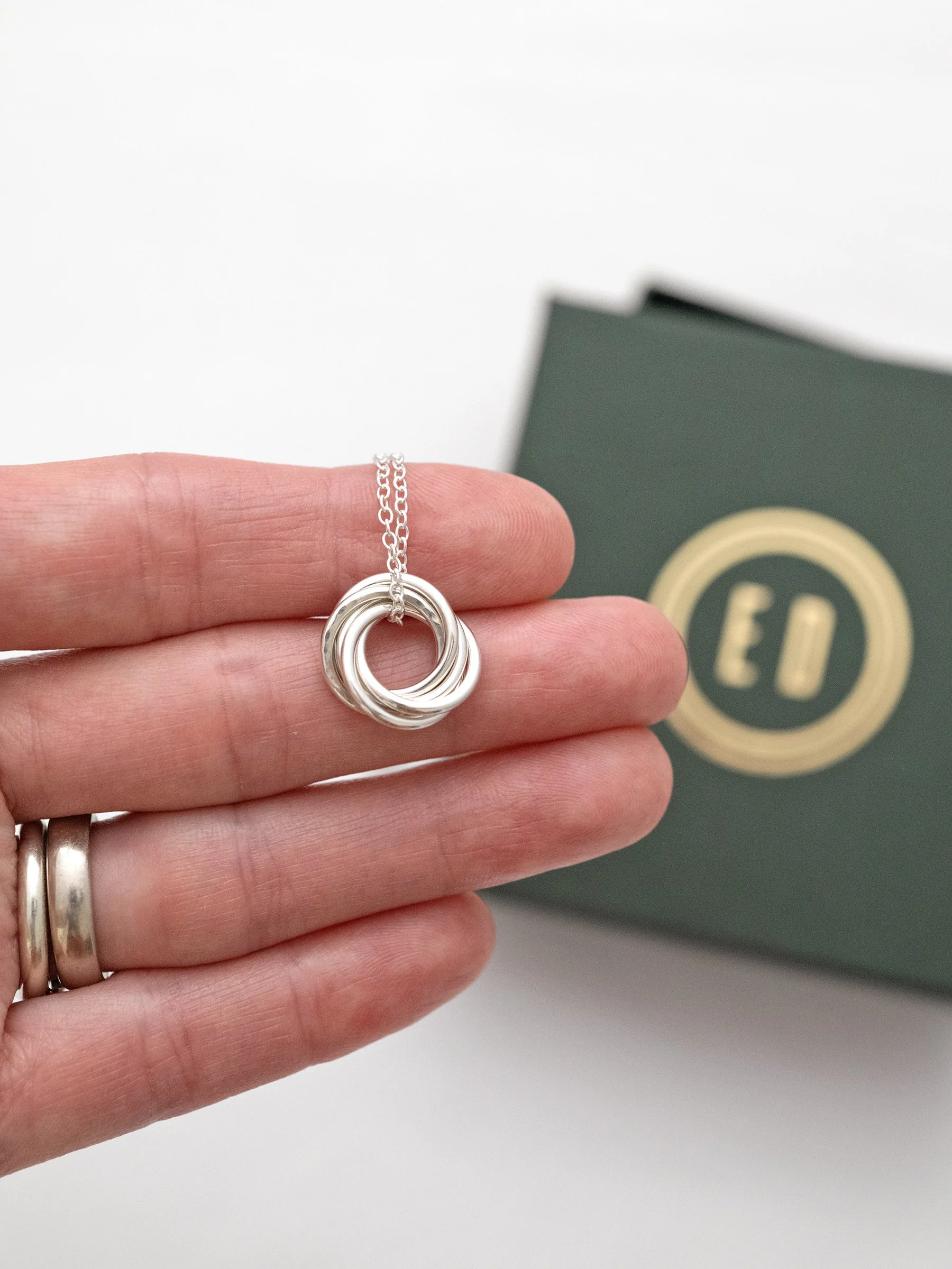 A sterling silver 50th necklace displayed in a persons hand with an Elizabeth Designs jewellery box in the background.