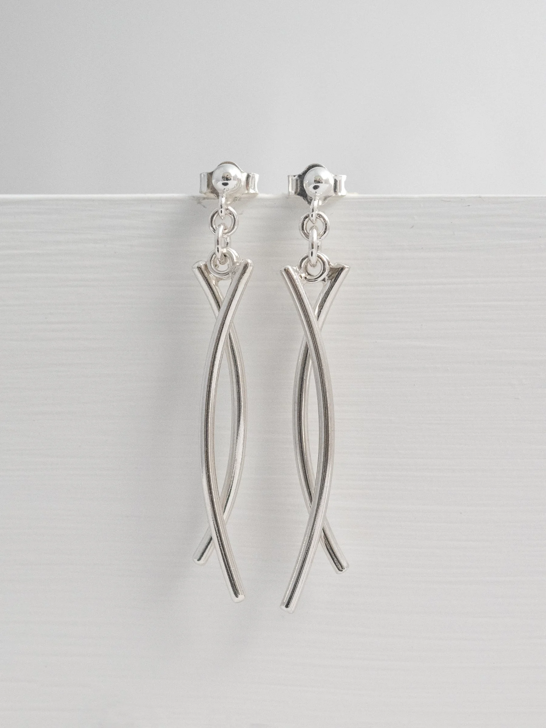A close up of sterling silver long dangle stud earrings hanging against a grey background.