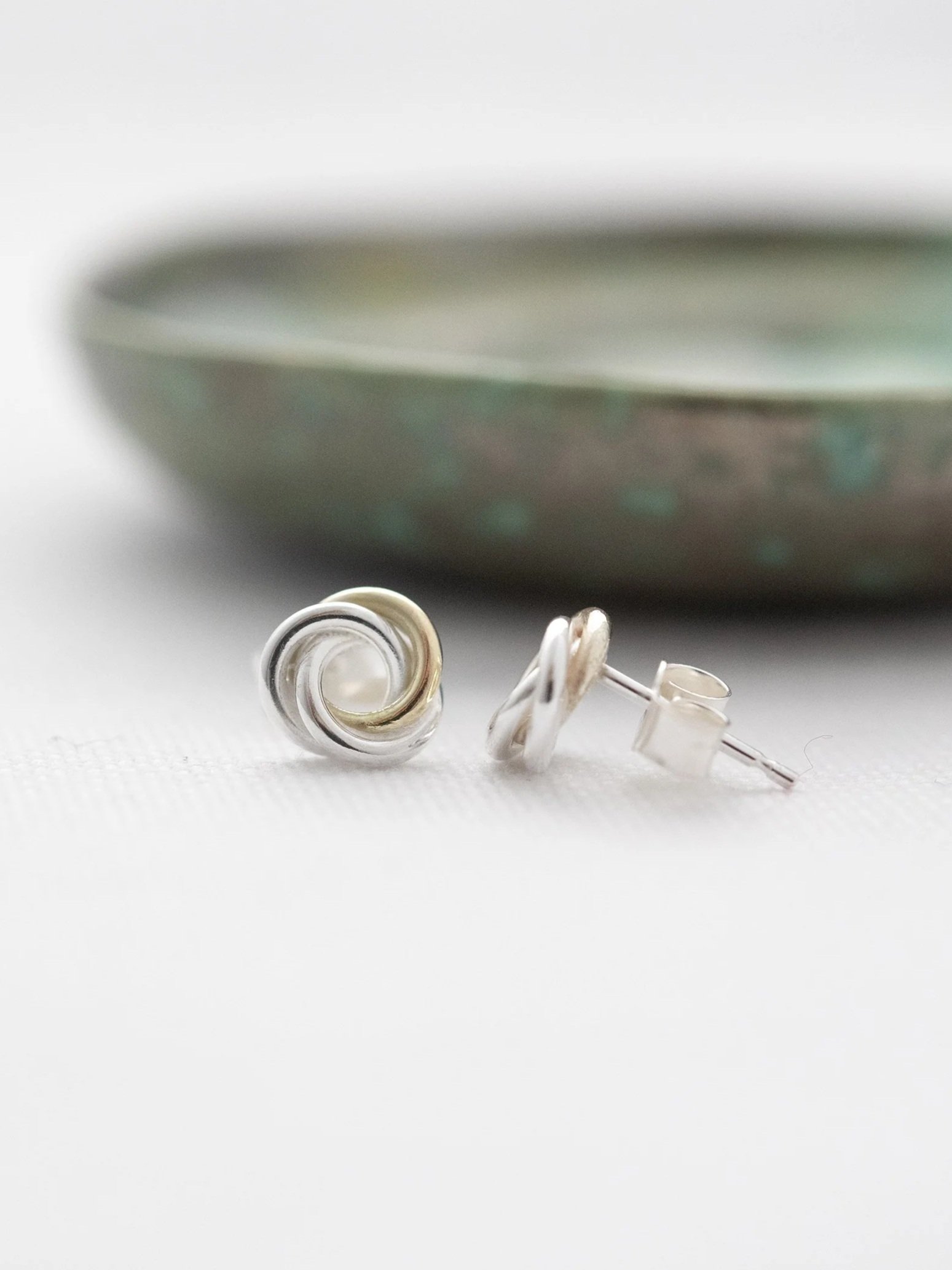 A front and side view of 9ct gold and silver circle stud earrings displayed on white material with a green jewellery dish in the background.